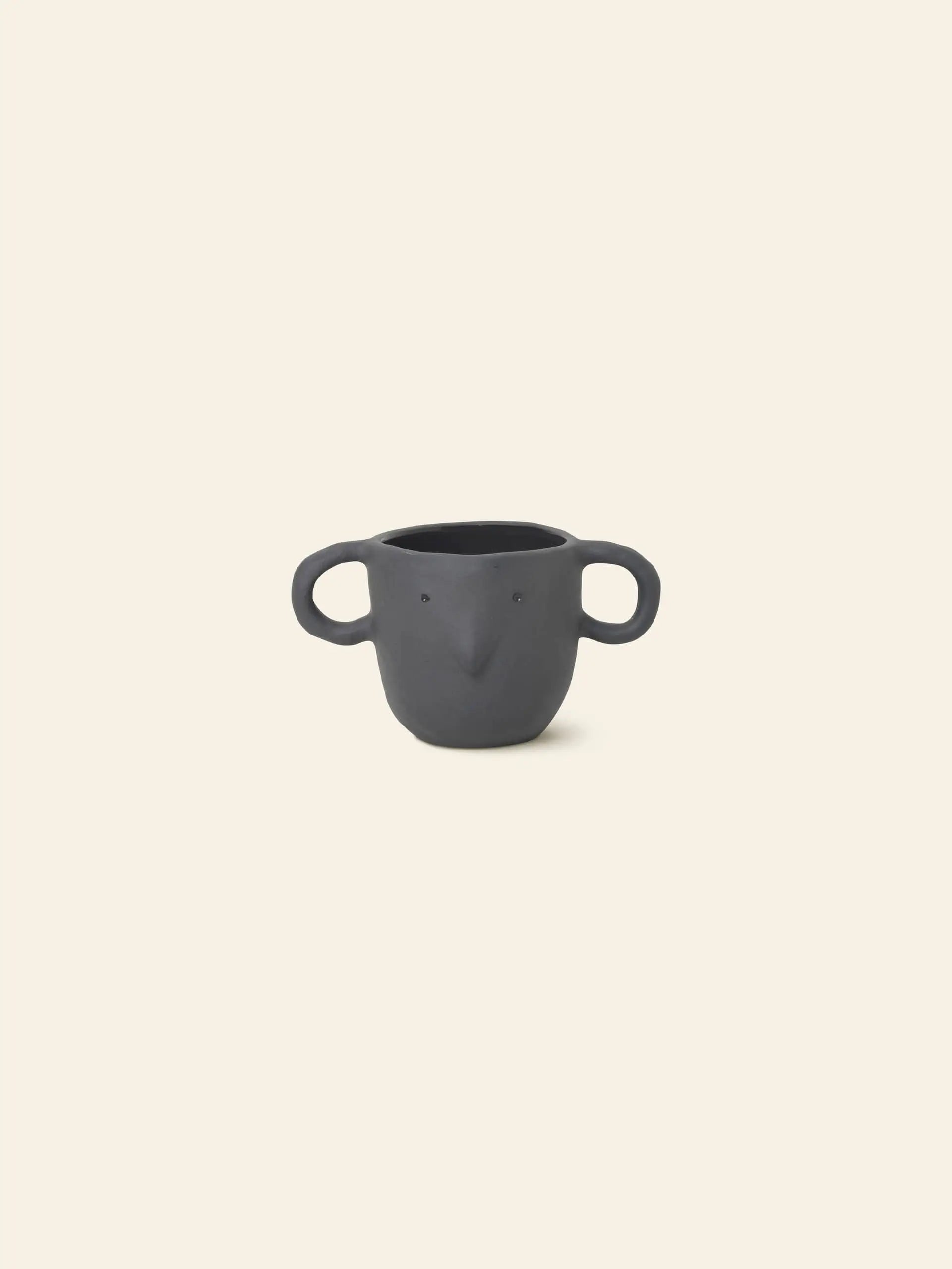 The ferm LIVING Mus Plant Pot, Small—black ceramic with mouse-ear handles and beak detail—features a whimsical animal-inspired design, perfect as a quirky plant pot and showcasing signature ferm LIVING style against a beige backdrop.