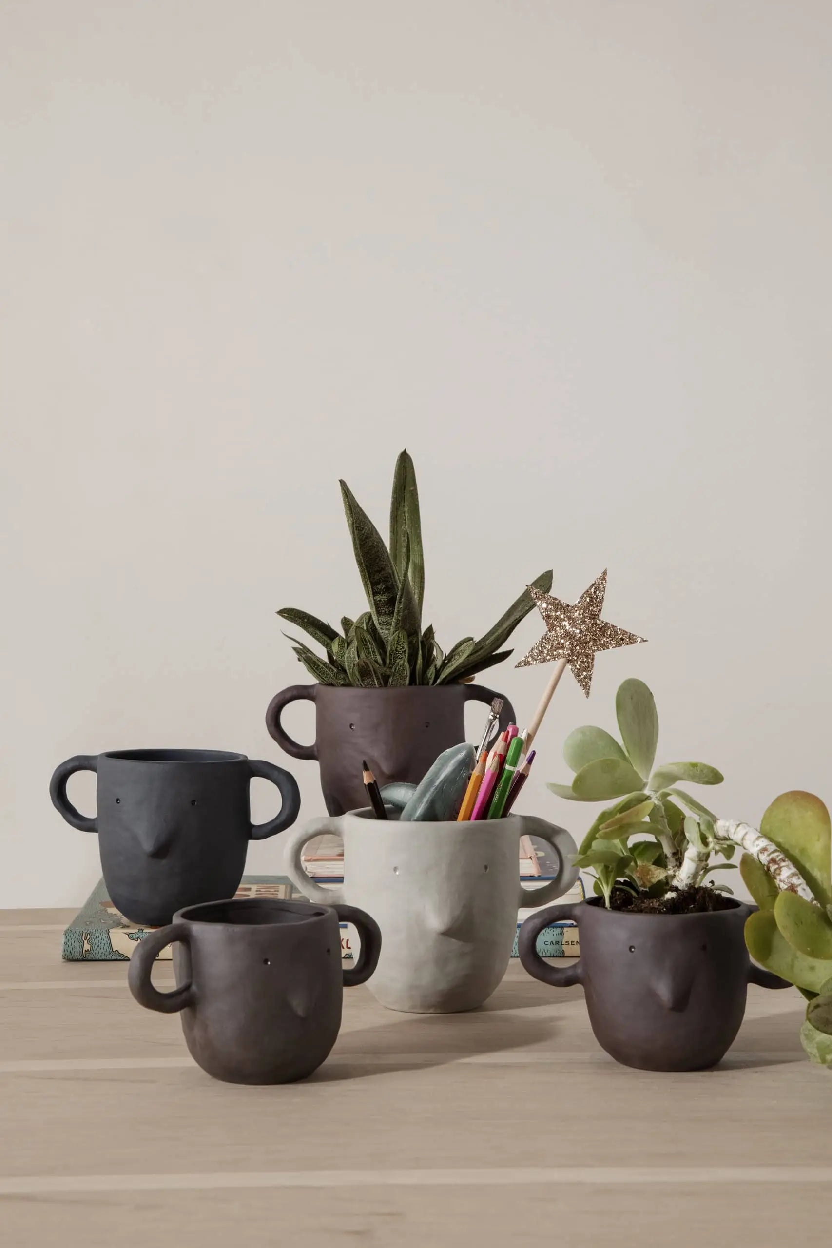 A set of five ferm LIVING Mus Plant Pots (Small), shaped like faces, are used as planters and a pen holder on a light wooden table—ideal for fans of ferm LIVING—set against a neutral background.