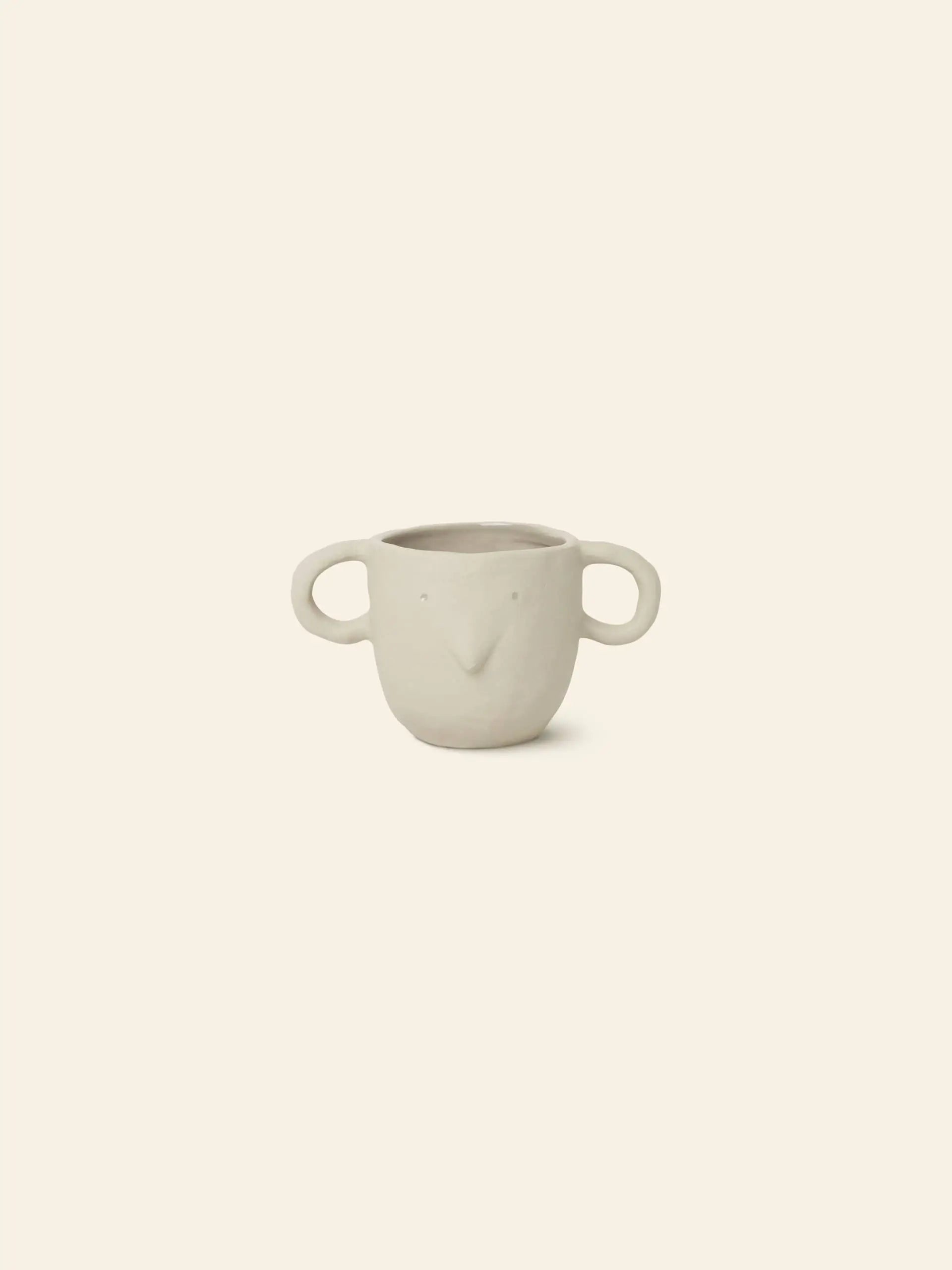 The ferm LIVING Mus Plant Pot, Small, is an off-white ceramic pot with two mouse-ear handles and minimal dot eyes and a v-shaped nose—perfect as a charming accent piece. Pictured on a simple beige background.