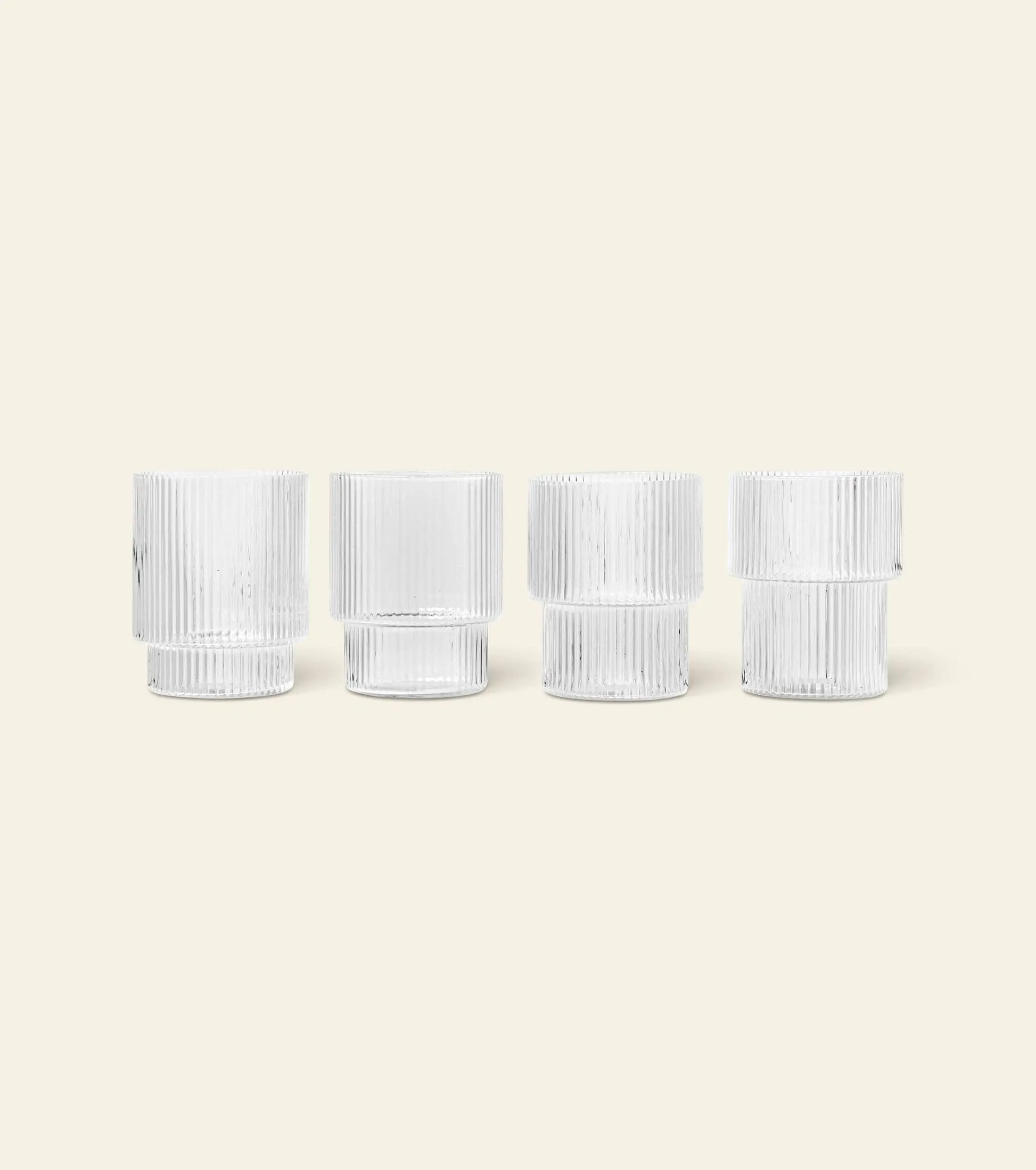 The ferm LIVING Ripple Drinking Glasses, Set of 4, feature a vertical ribbed texture and are shown side by side against a light beige background—an elegant addition to any glassware collection.