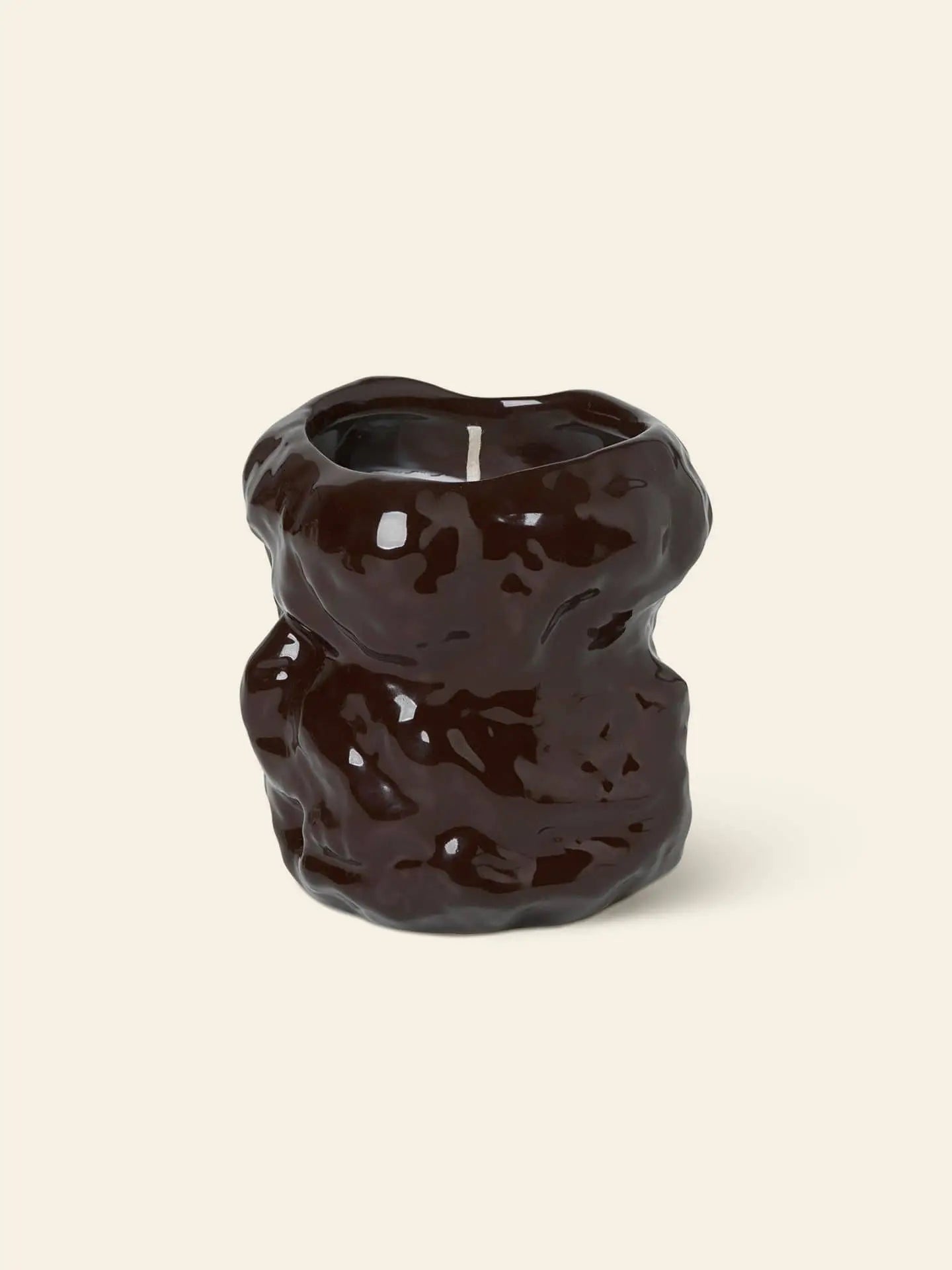 The ferm LIVING Tuck Scented Candle features a glossy, dark brown stoneware design with wavy, organic lines, creating a calming ambiance against a light beige background.