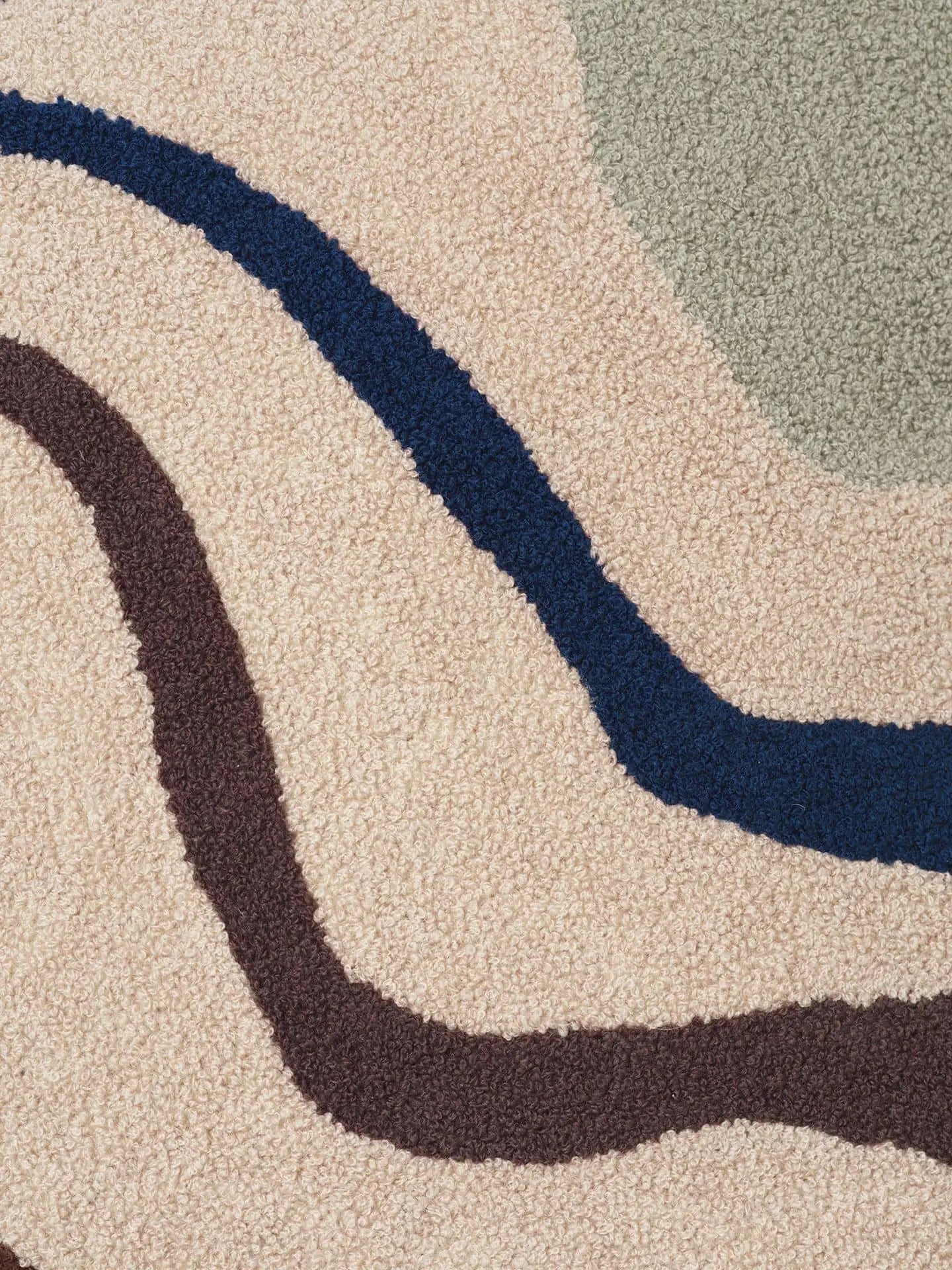 A close-up of a textured beige carpet with wavy dark brown, navy blue, and light gray lines creates a modern look, ideal for luxury homes or pairing with the ferm LIVING Vista Cushion by ferm LIVING.