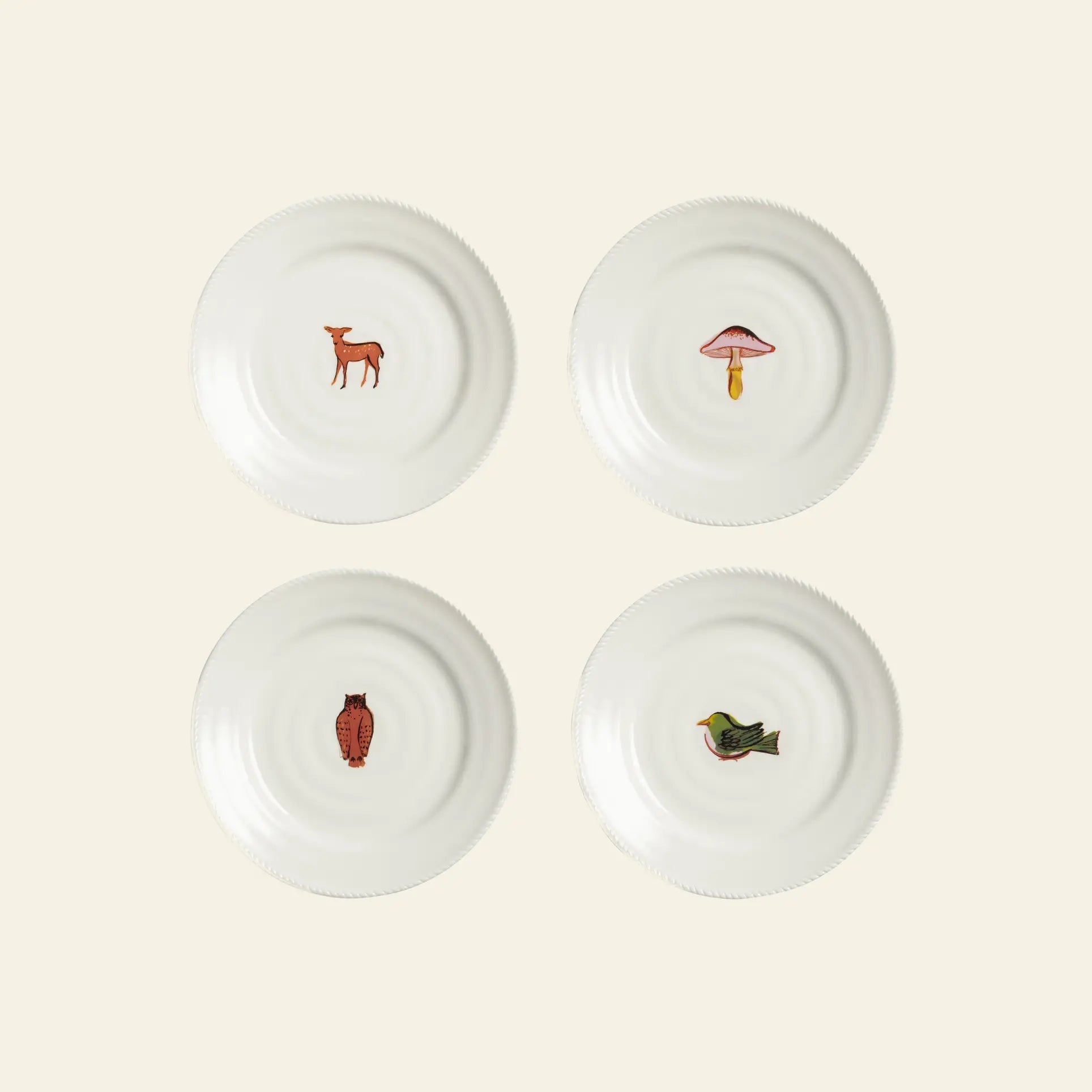 The &klevering Autumn Plate Small, Set of 4 by &klevering features white ceramic plates with nature-inspired prints—a deer, mushroom, owl, and bird—centered on an autumn-themed backdrop. Perfect for charming table settings.