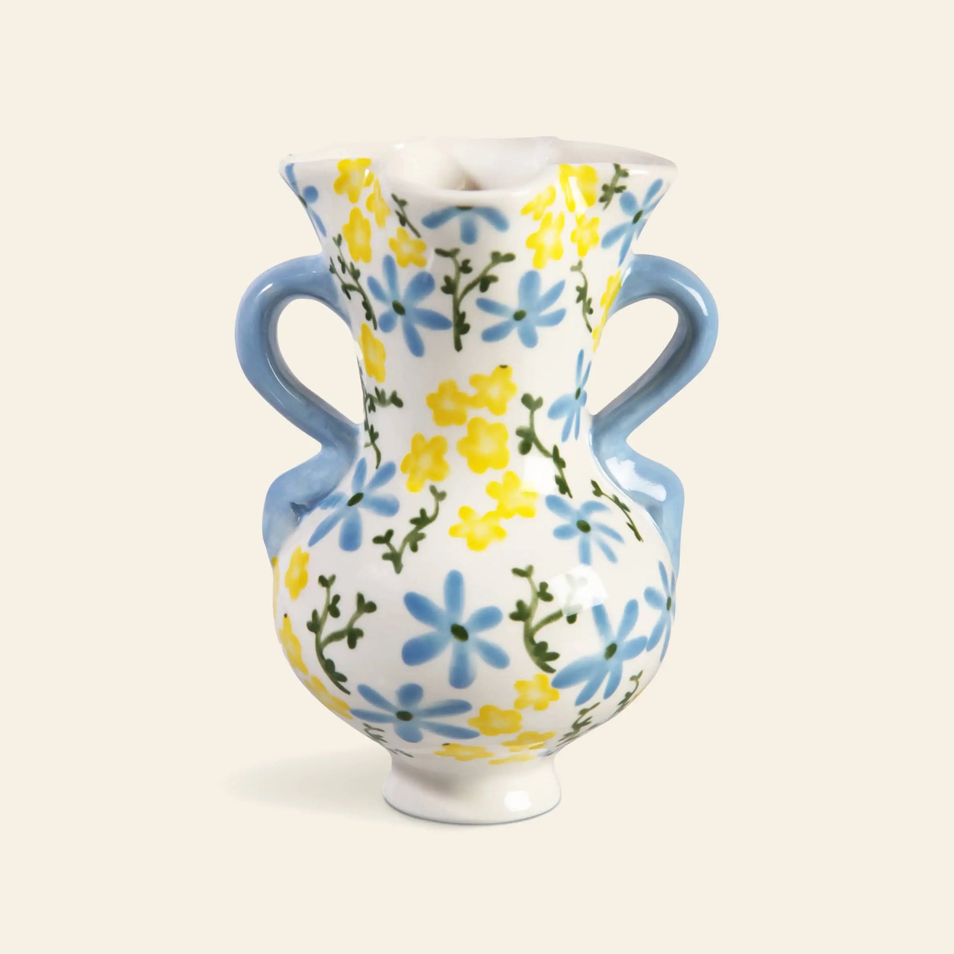 The &klevering Buttercup Vase by &klevering features a classic curvy shape with two blue handles, a flared rim, and hand-painted blue and yellow petite flowers with green stems on a white ceramic background.