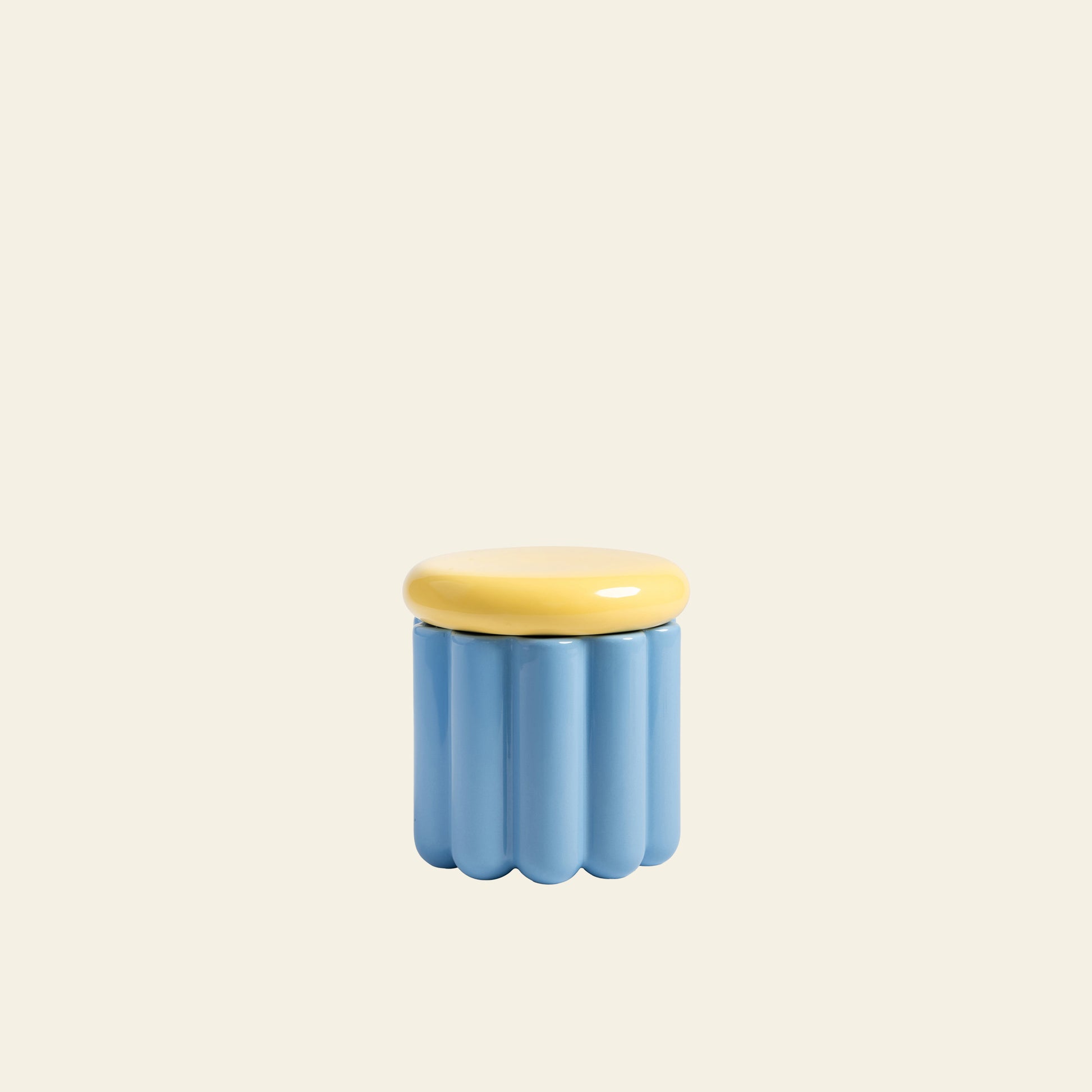 The &klevering Charlo Jar - Blue by &klevering is a small, light blue ceramic container with a wavy ridged design and a smooth round yellow lid with an airtight silicone seal, shown against an off-white background.