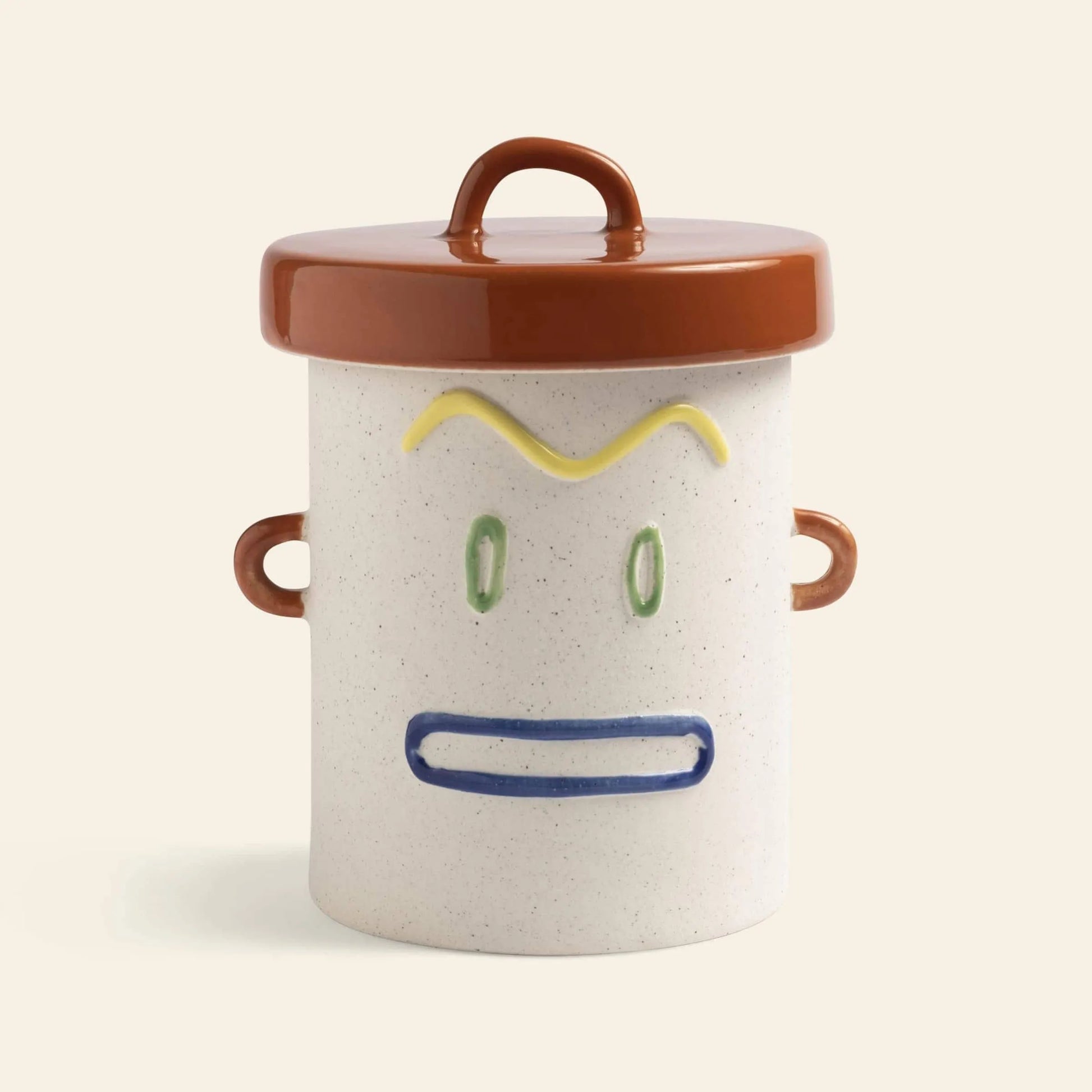 The &klevering Cheeky Jar by &klevering features a playful ceramic design with a brown lid and handles, sporting yellow eyebrows, green eyes, and a blue mouth—a charming storage companion for any shelf.