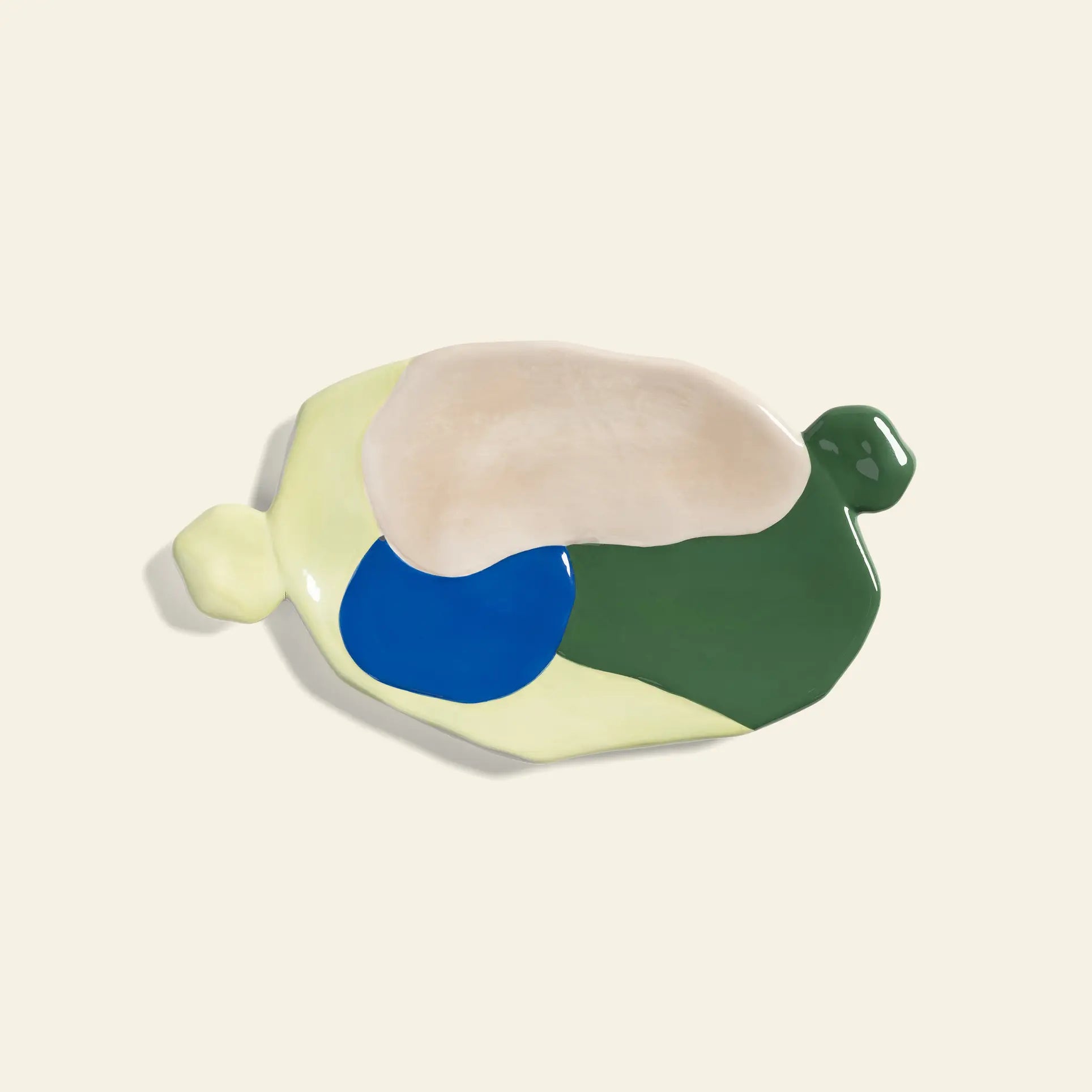 The &klevering Chunky Platter, Medium by &klevering features an artistic, irregular ceramic shape with glossy cream, dark green, blue, and pale yellow patches on light beige and two small raised knobs on opposite sides.