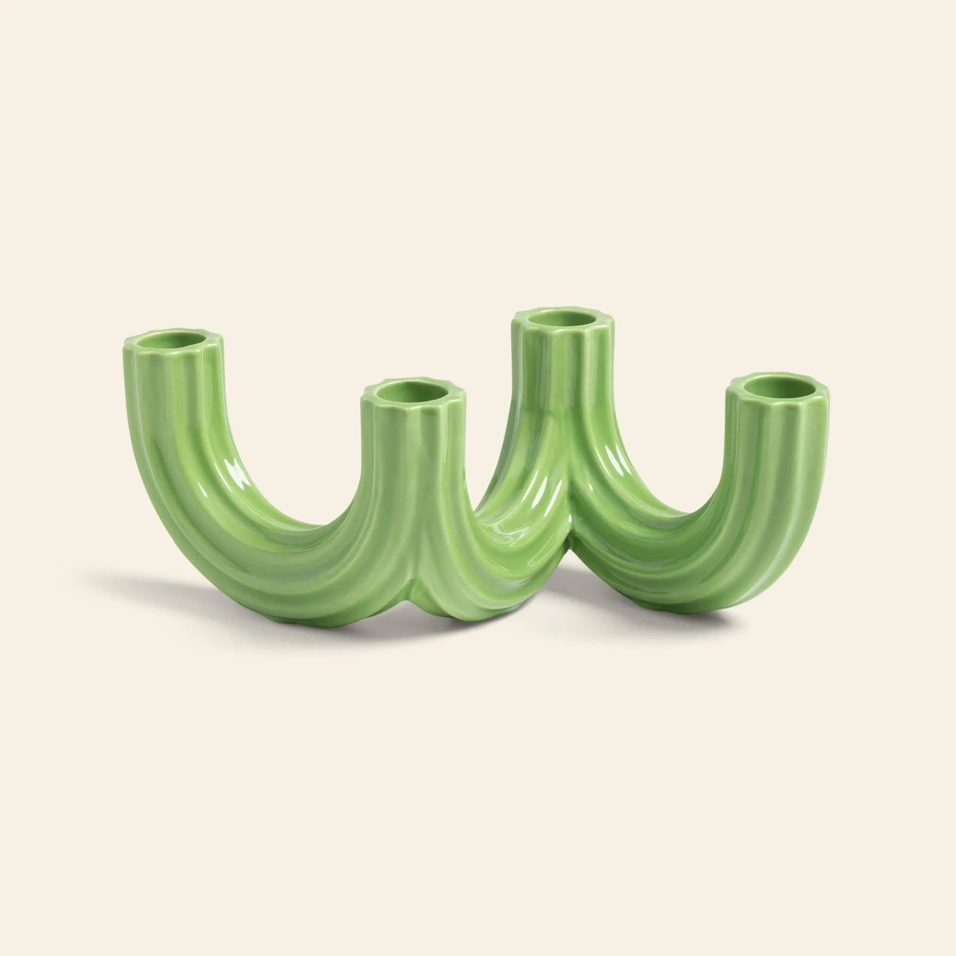 The &klevering Churros Candle Holder Green by &klevering features four glossy, curved U-shaped tubes joined at the base, creating a unique home decor accent, shown against an off-white background.