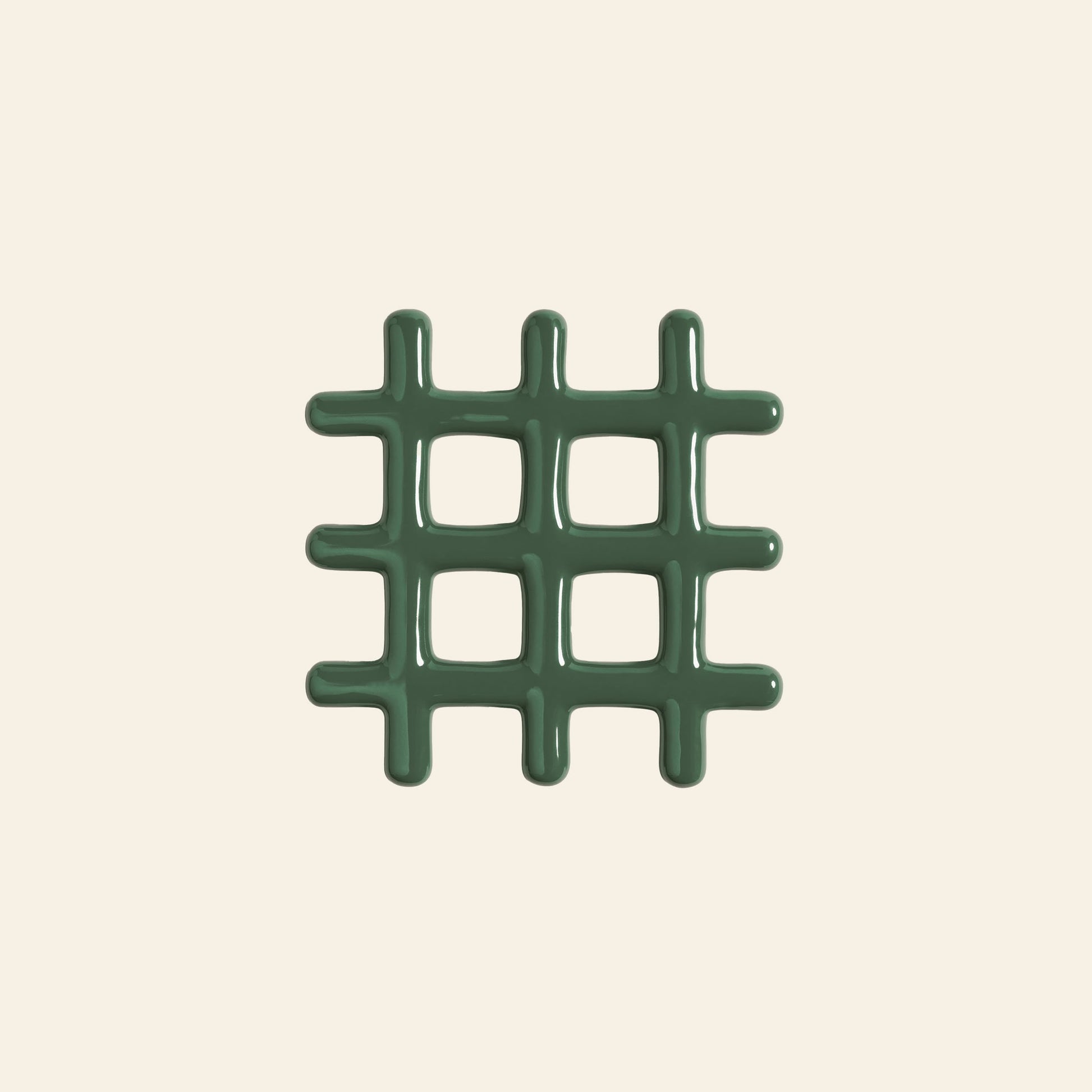 The &klevering Grid Trivet by &klevering is a green, glossy trivet with a geometric design, rounded edges, and four square openings. It is centered on a plain, light beige background.