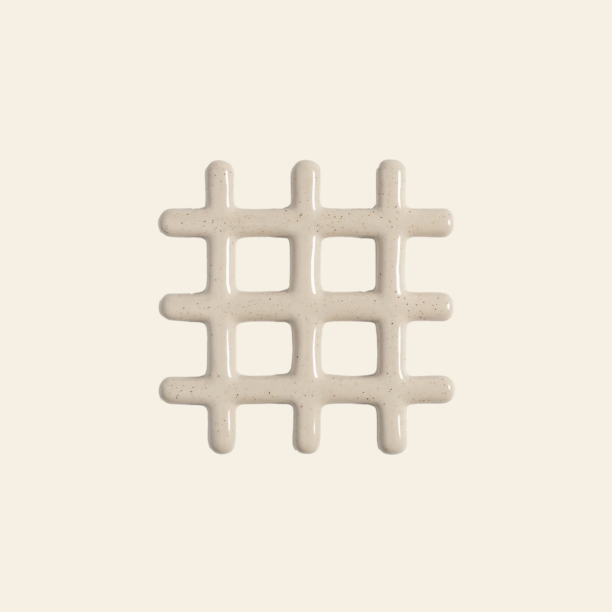 The &klevering Grid Trivet by &klevering features a shiny off-white, speckled grid design that resembles icing on a light beige background. This stylish trivet adds visual appeal while protecting surfaces from heat.