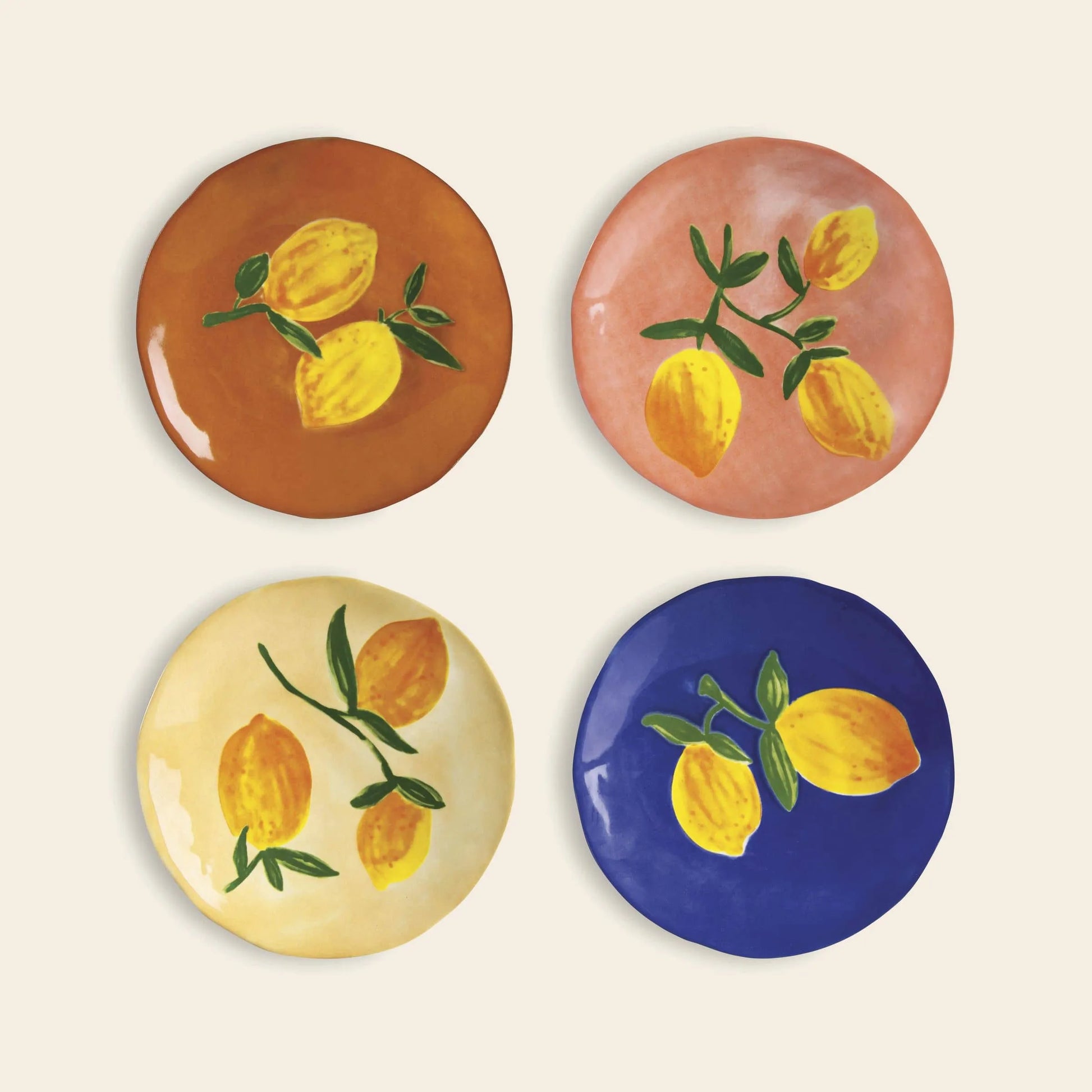The &klevering Lemon Plate, Set of 4 features plates in brown, pink, cream, and blue with painted yellow lemons and green leaves. These uniquely shaped &klevering plates are perfect for a fresh summer table setting. Displayed in a 2x2 grid on a light background.