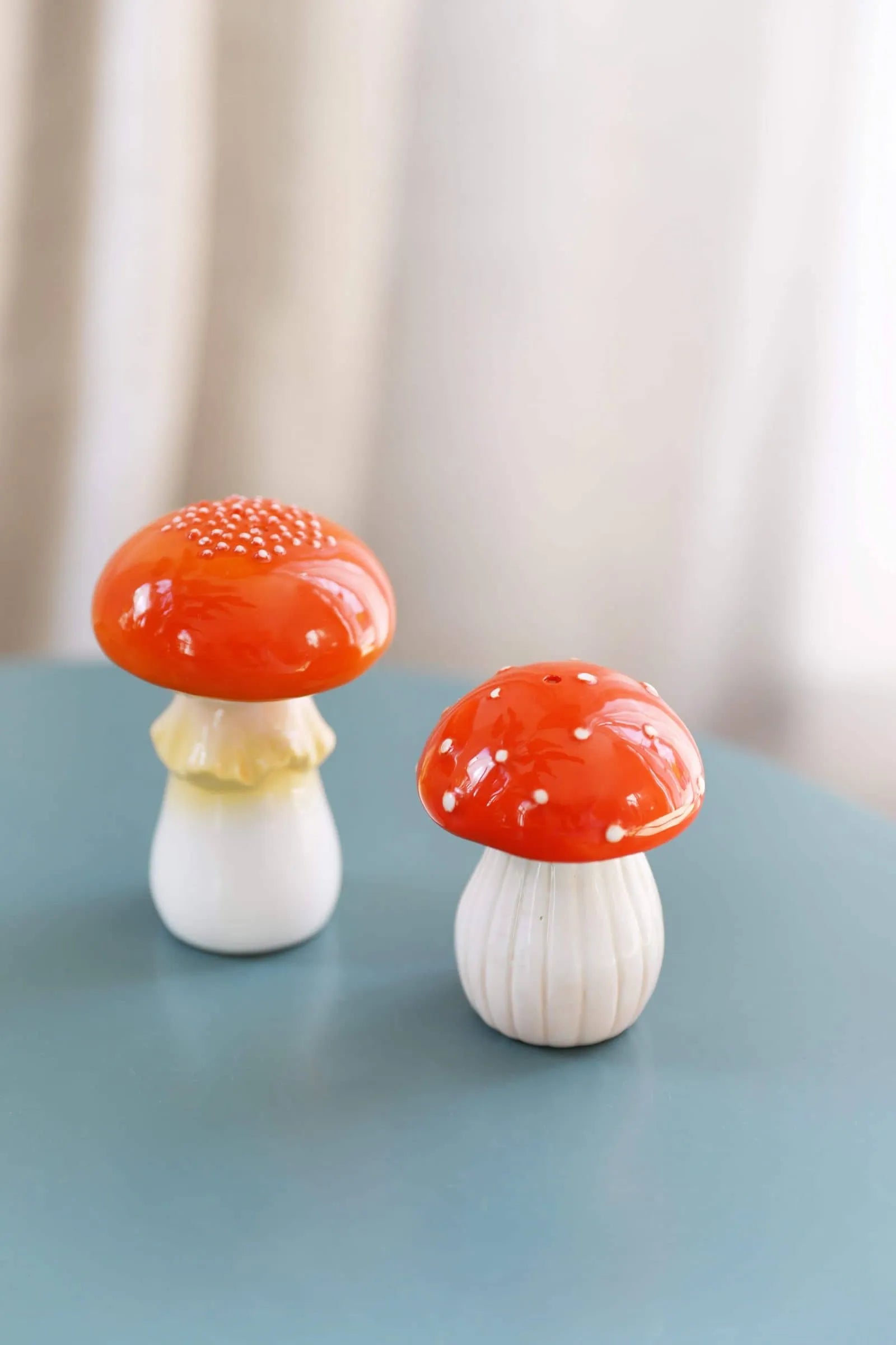 The &klevering Mushroom Salt & Pepper Set features two ceramic figurines with red caps and white stems, one with a wide dotted cap and the other taller with a yellow-tinted stemโperfect for whimsical kitchen decor.