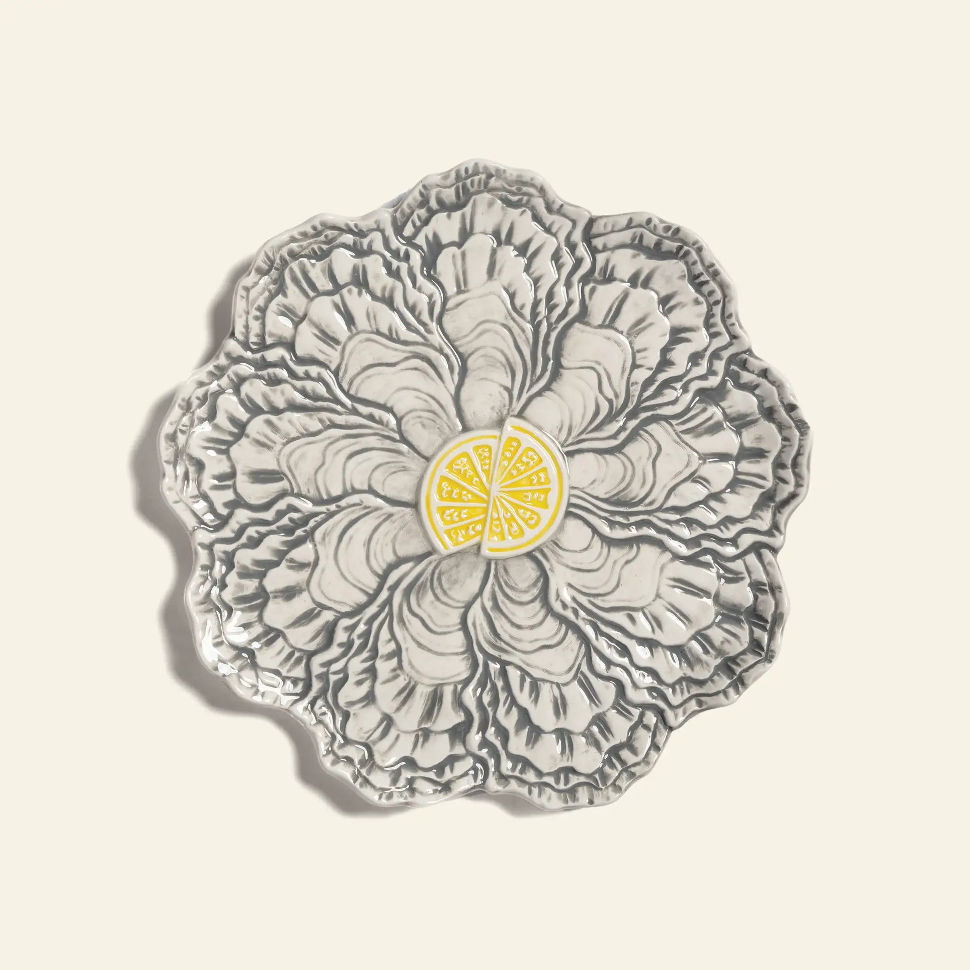 The &klevering Oyster Plate by &klevering is a decorative gray ceramic plate shaped like layered oyster shells with detailed ridges and a central yellow lemon wedge design—ideal for serving oysters. Photographed on a plain, light background.