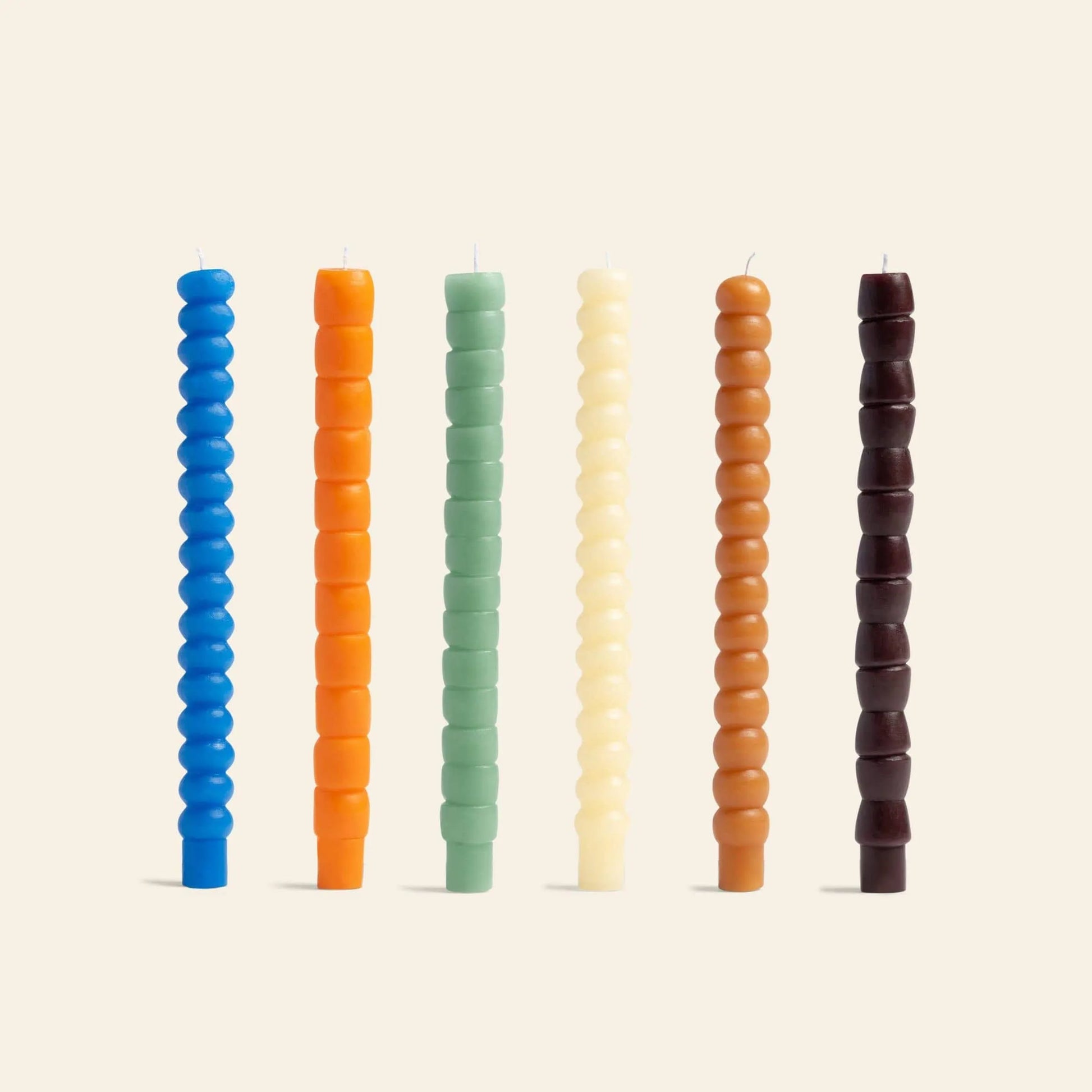 The &klevering Pebble Candle Set includes six tall, handcrafted candles in blue, orange, green, cream, brown, and dark brown with geometric texture by &klevering, arranged vertically on a light beige background.