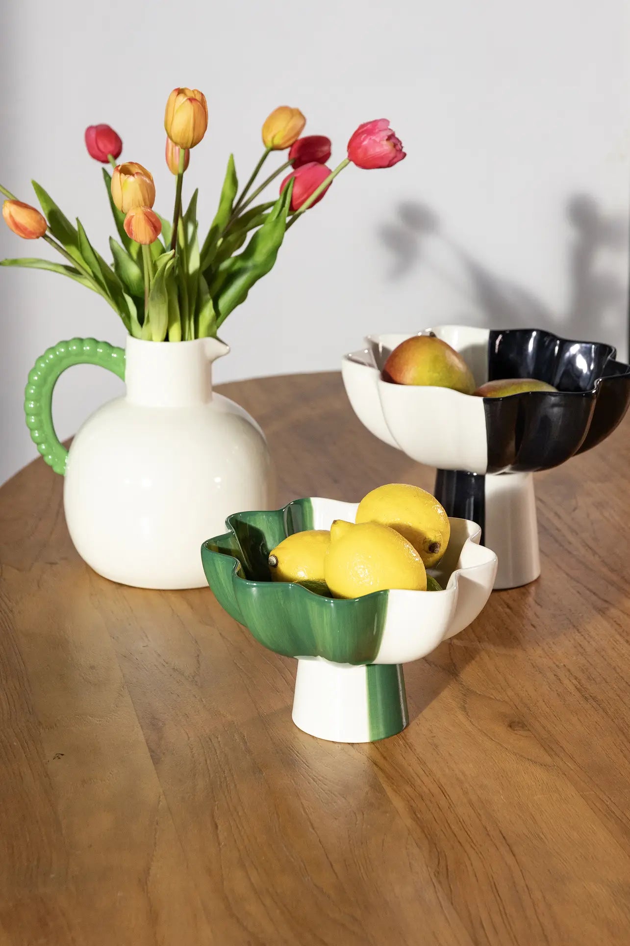 An elegant wooden table features the &klevering Perle Jug filled with pink and orange tulips, plus two flower-shaped ceramic bowls—one green with lemons, another black and white with apples and pears—ideal for summer dining.