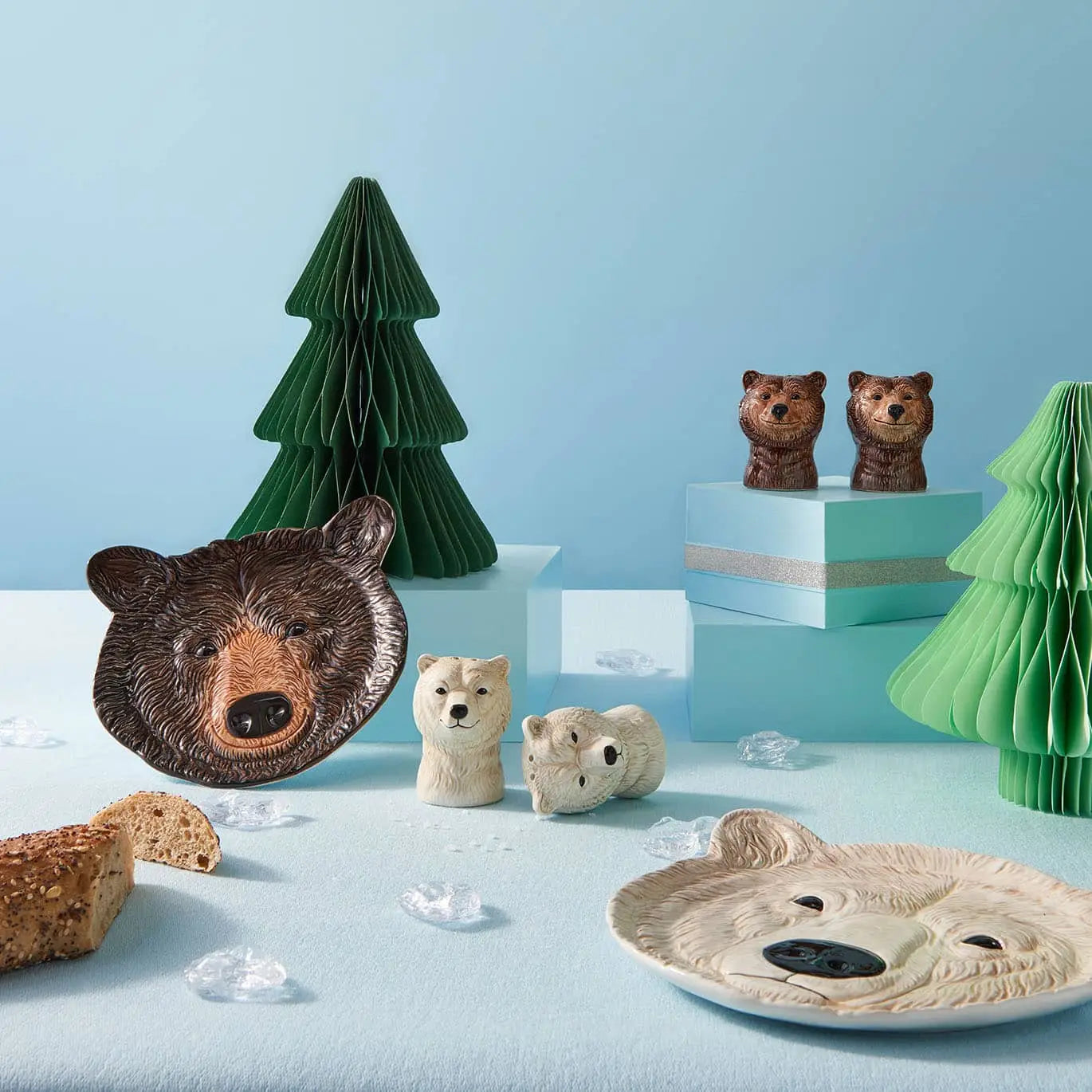 A charming table setting showcases &klevering’s Polar Bear Salt & Pepper Set, polar bear face plates, green paper trees, and faux ice—all artfully arranged on a pale blue surface with a slice of bread.