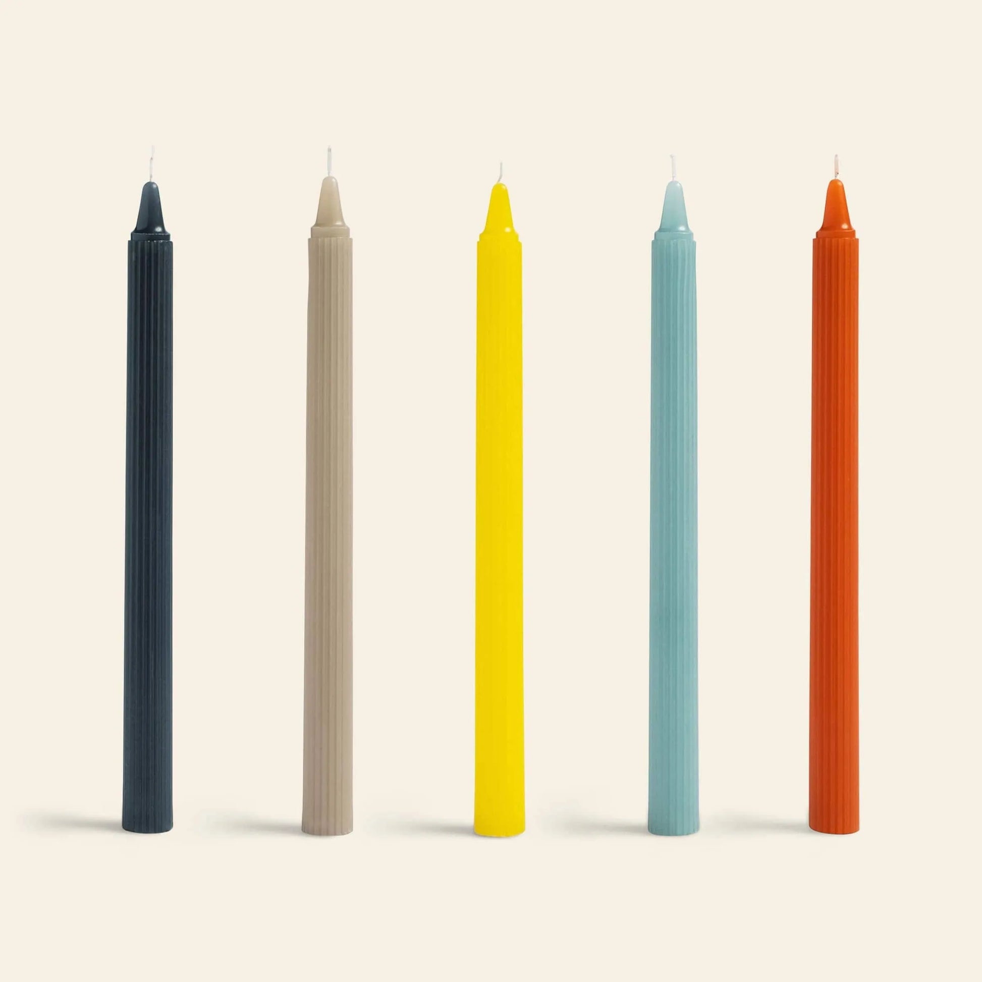 The &klevering Ripple Candle Set of 5 features tall black, beige, yellow, light blue, and orange candles with a modern vertical lined texture, all standing upright in a row against a light background.