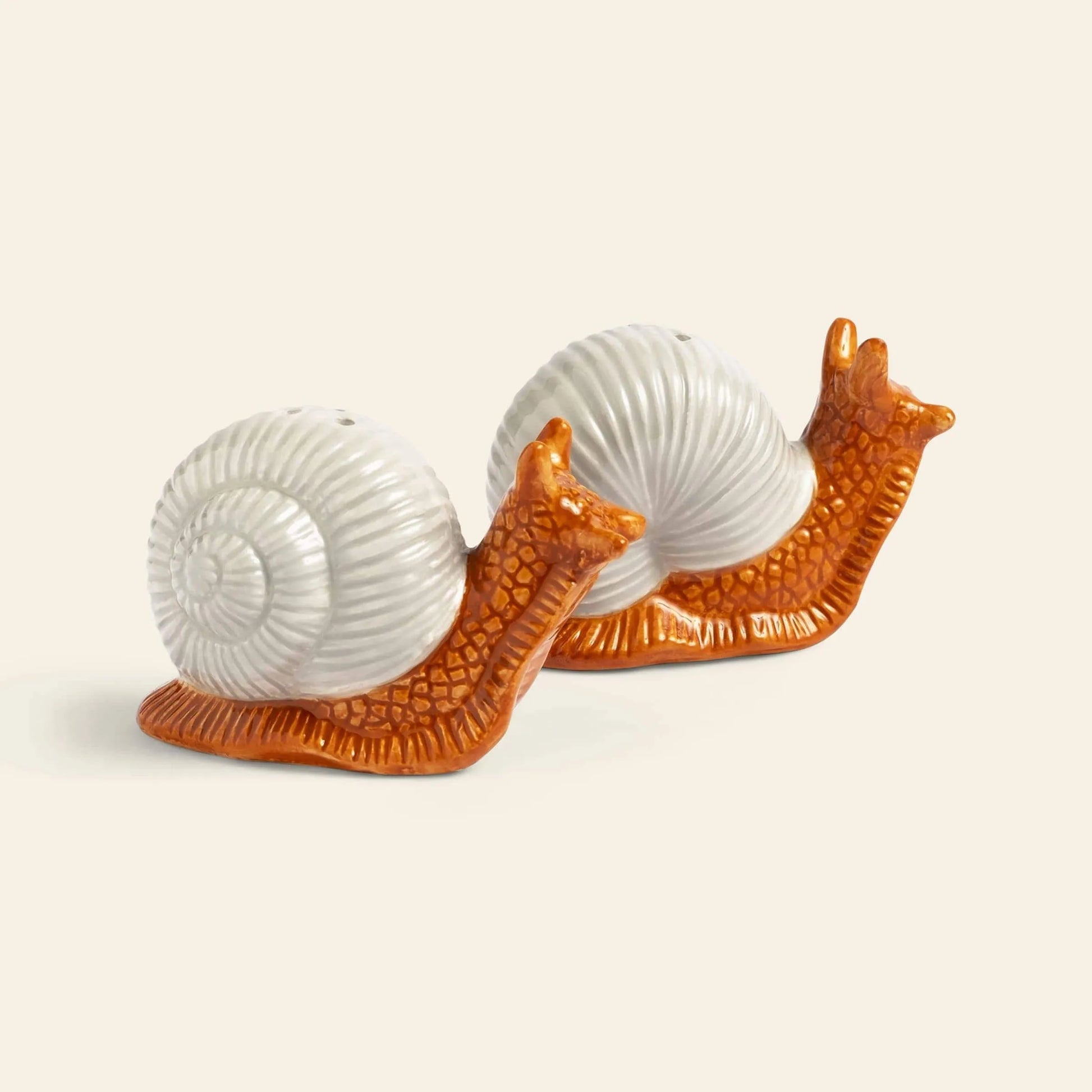 The &klevering Snail Salt & Pepper Set by &klevering features two ceramic snail-shaped figurines in white and orange, side by side on a light background, adding a whimsical touch to your table setting.