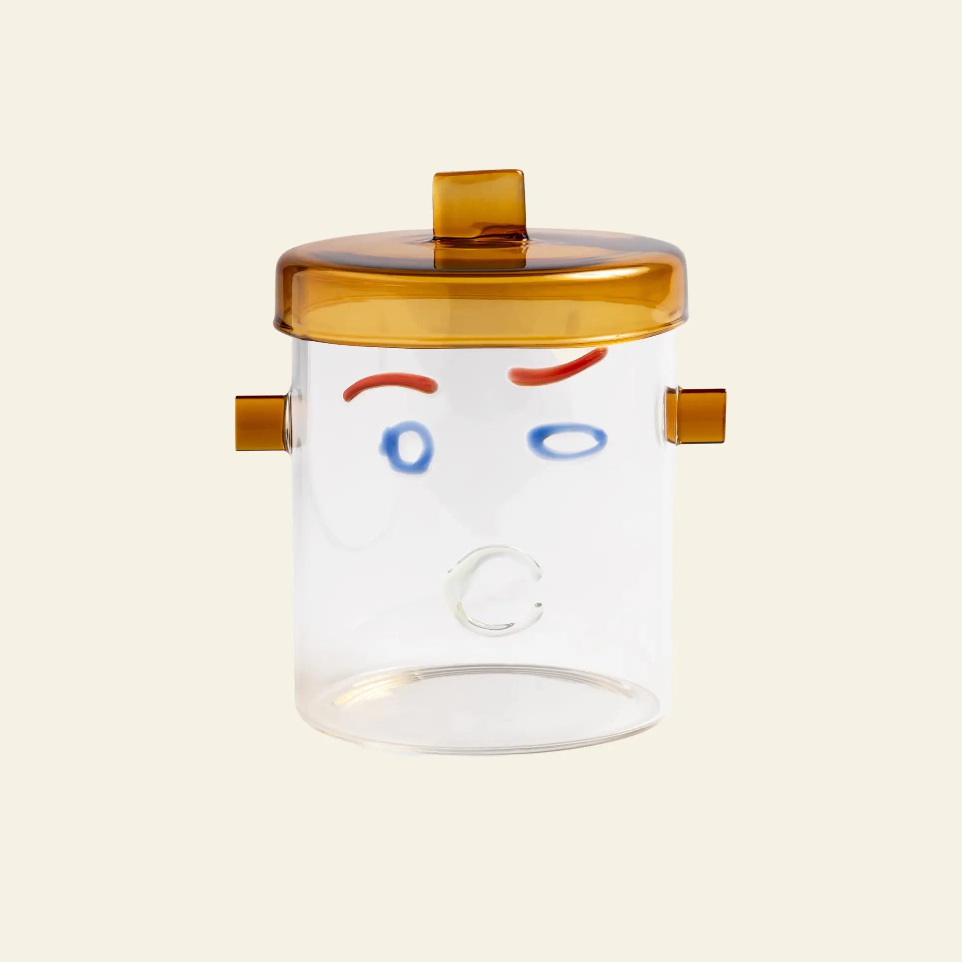 The &klevering Surprised Jar by &klevering is a colourful transparent glass jar with a stylish handle, amber lid, and abstract lines depicting a playful face with red eyebrows, blue eyes, and a circular mouth.