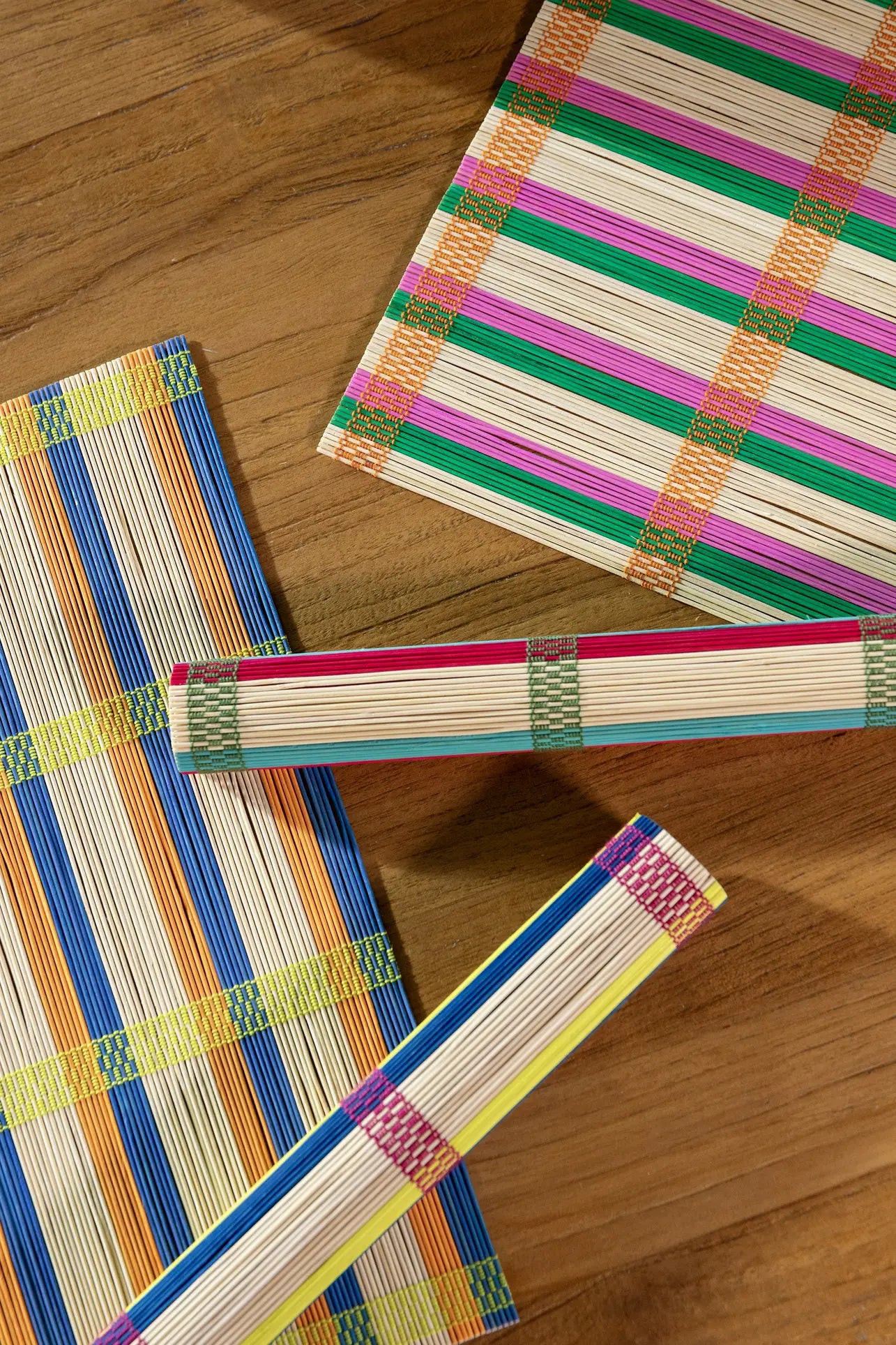 The &klevering Umami Placemat Set of 4 features colorful striped bamboo designs in blue, green, orange, pink, and yellow—two rolled up and two flat—ideal for adding vibrant style to your dining table.