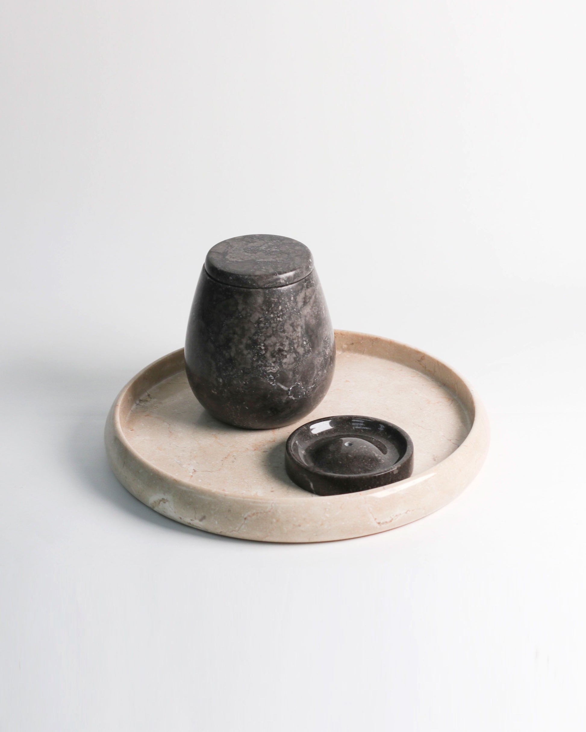 The stillgoods Ebb Incense Holder—a dark, rounded stone jar with lid and flat dish—rests on a circular, light marble tray, ideal as an accessory tray or incense holder, displayed against a plain white background.