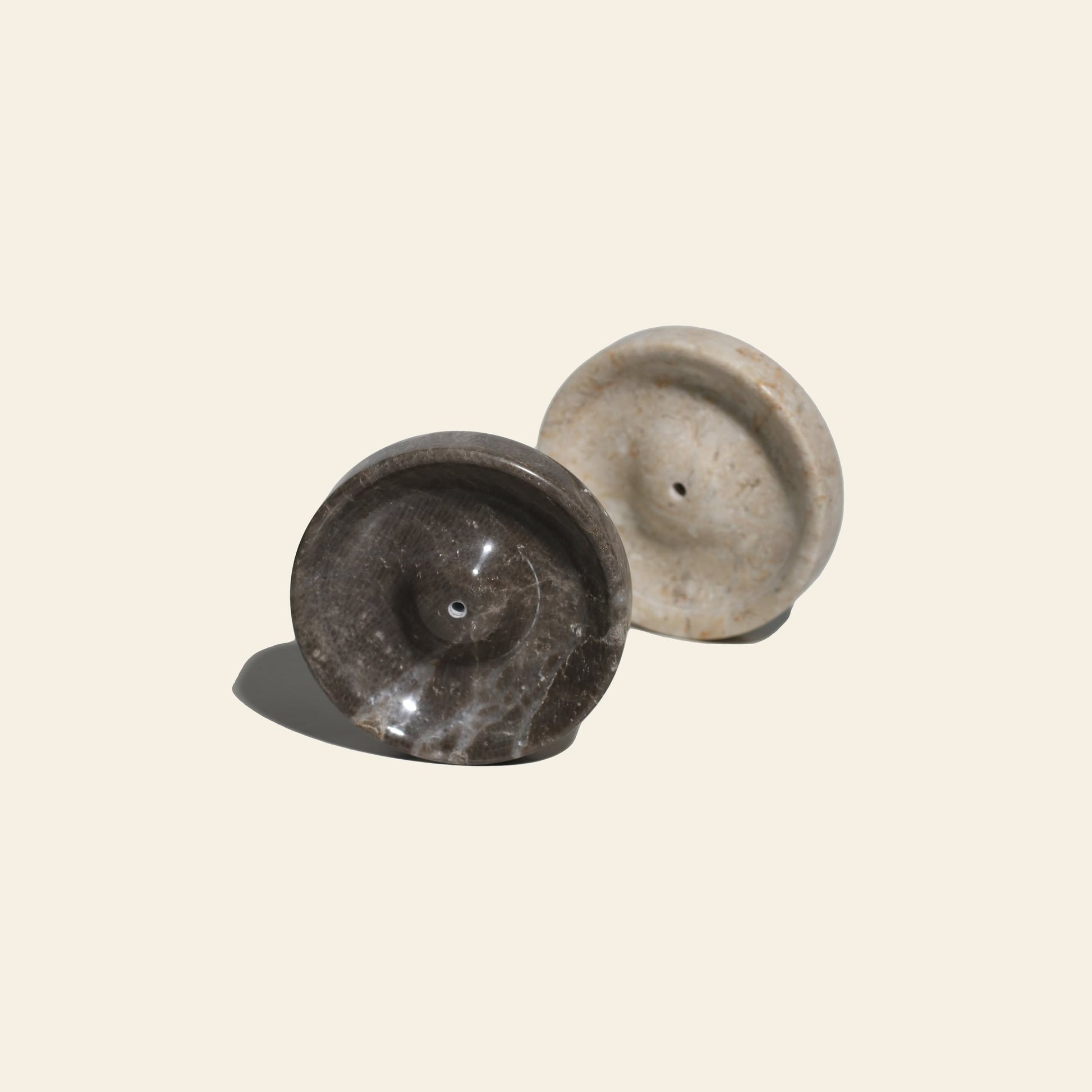 Two round stillgoods Ebb Incense Holders—one dark brown, one light beige—stand upright on a light background. Made by stillgoods, these minimalist stone pieces serve as incense holders or chic accessory trays.