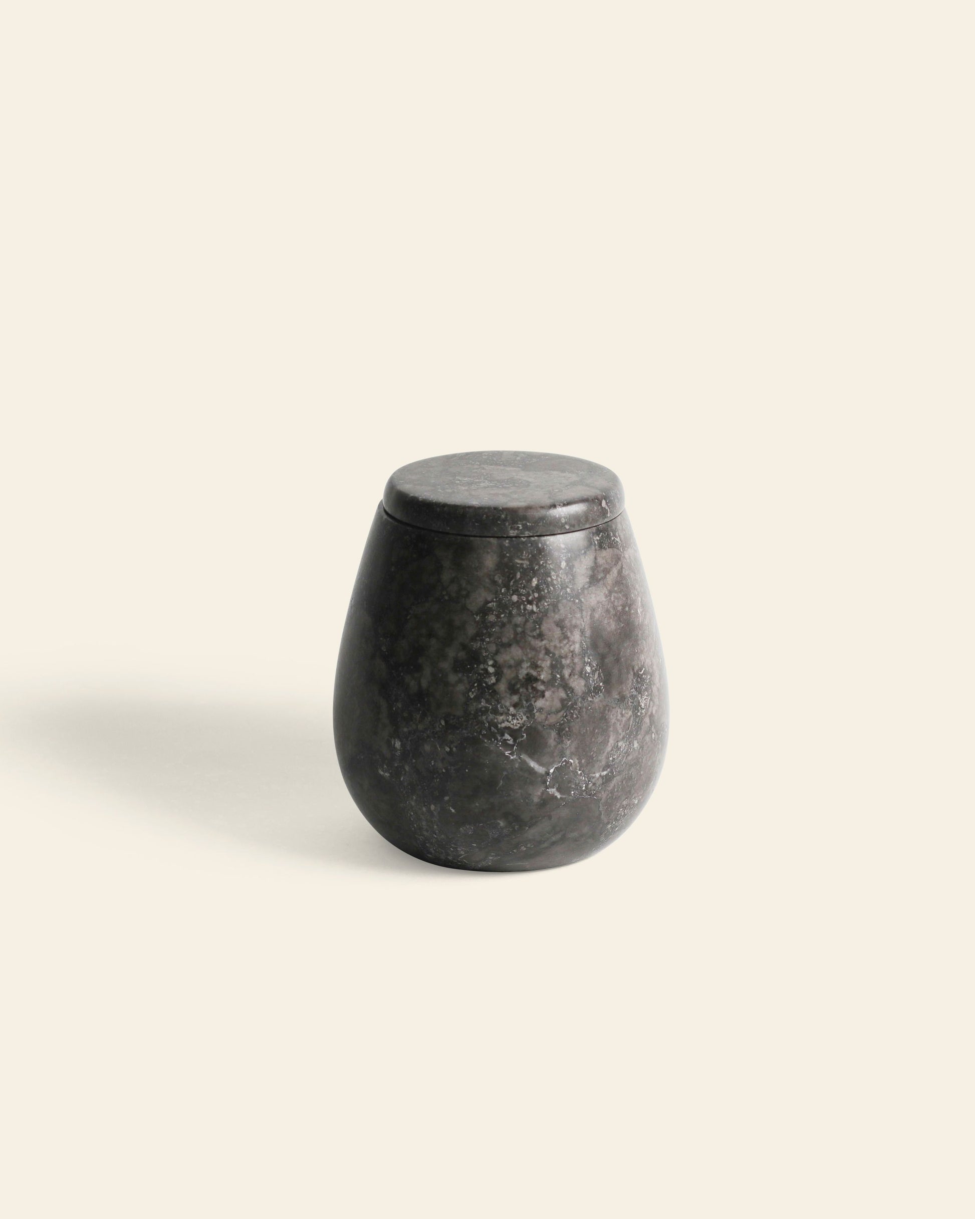 The stillgoods Ecru Jar by stillgoods features a dark, rounded marble design with a matching lid, perfect for organizing or storing condiments, pictured on a plain light beige background.