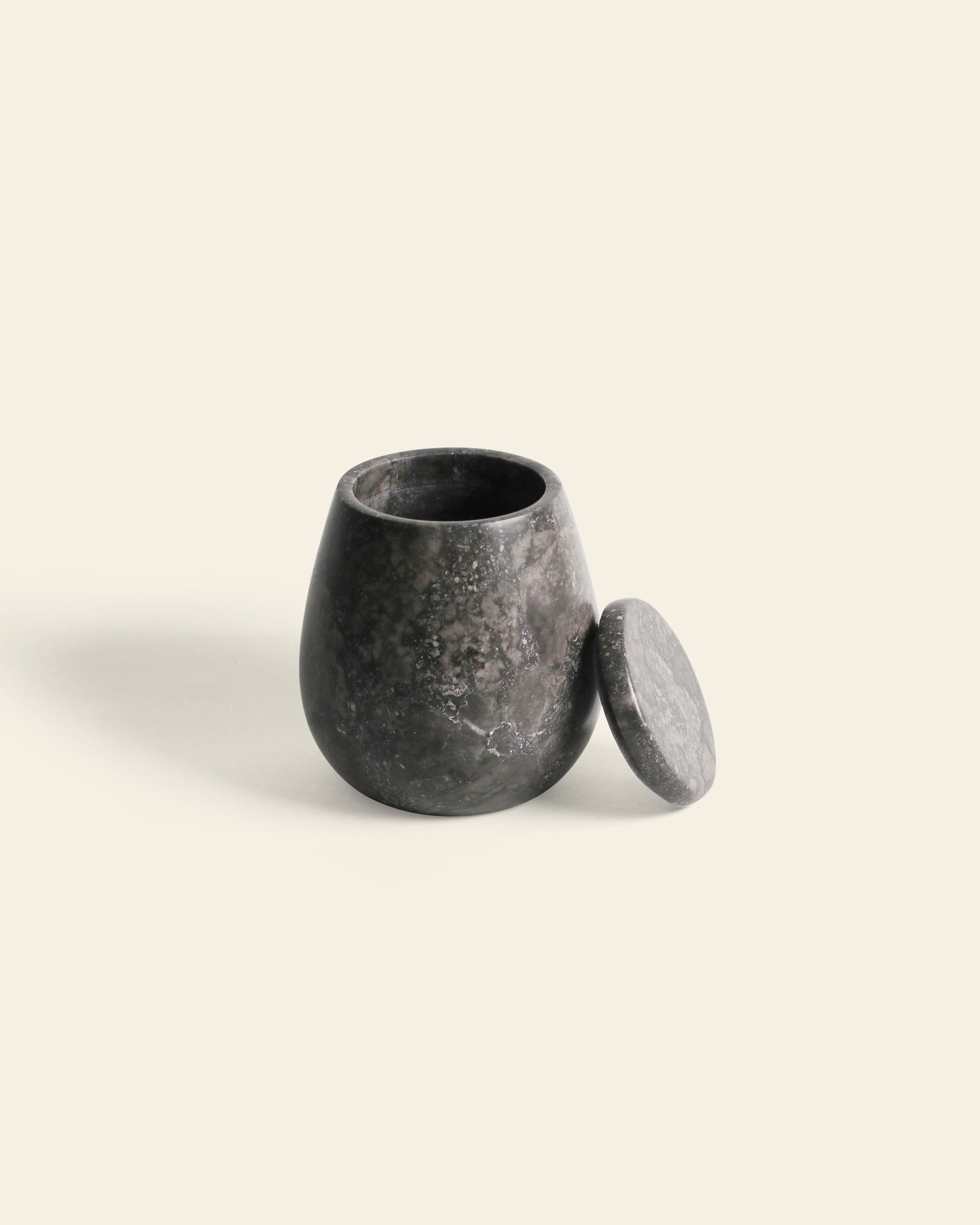 The stillgoods Ecru Jar, a small, rounded black marble container with a removable lid, is ideal for storing condiments or organizing essentials, shown here against a cream-colored background.