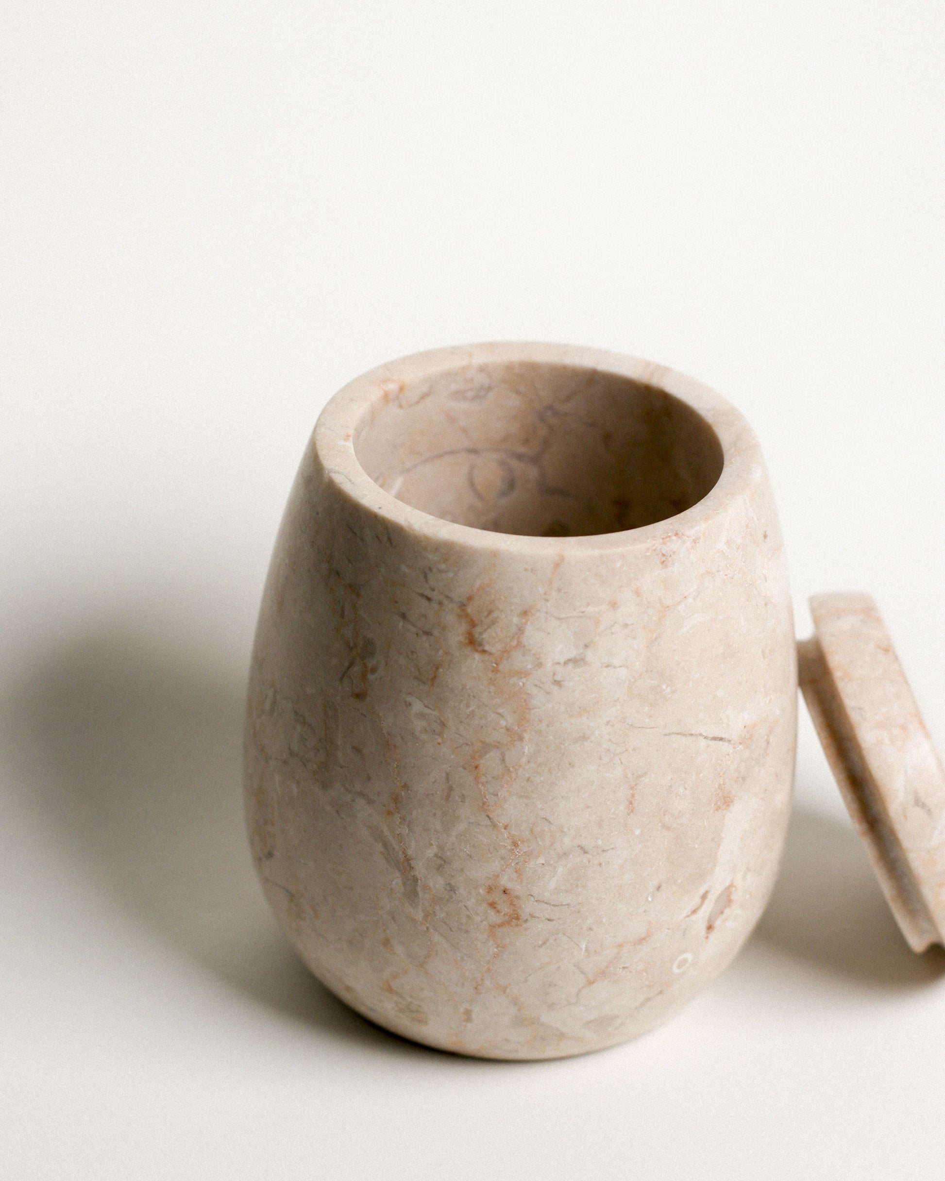 The stillgoods Ecru Jar features a smooth, polished finish with subtle veining. Set on a white surface with its matching lid, this stylish organizer by stillgoods is ideal for storing condiments or adding elegance to your countertop.