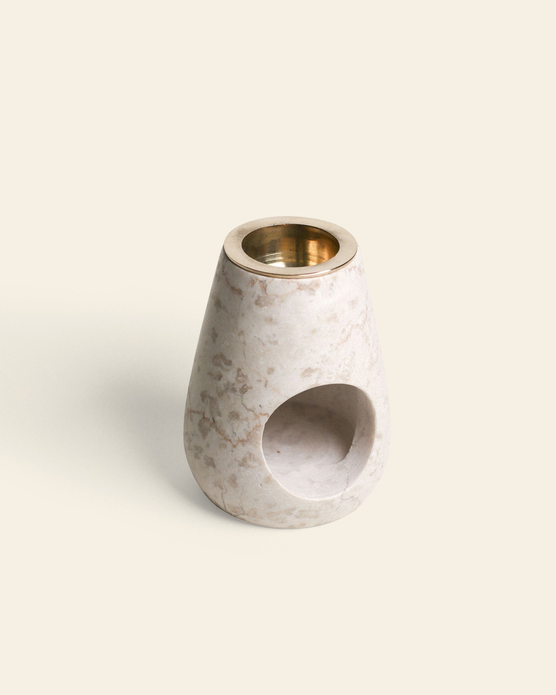 The stillgoods Eli Oil Burner features a small, cone-shaped marble design with a brass cup on top and a round side opening, ideal for creating a calming scent. Shown against a plain, light background.