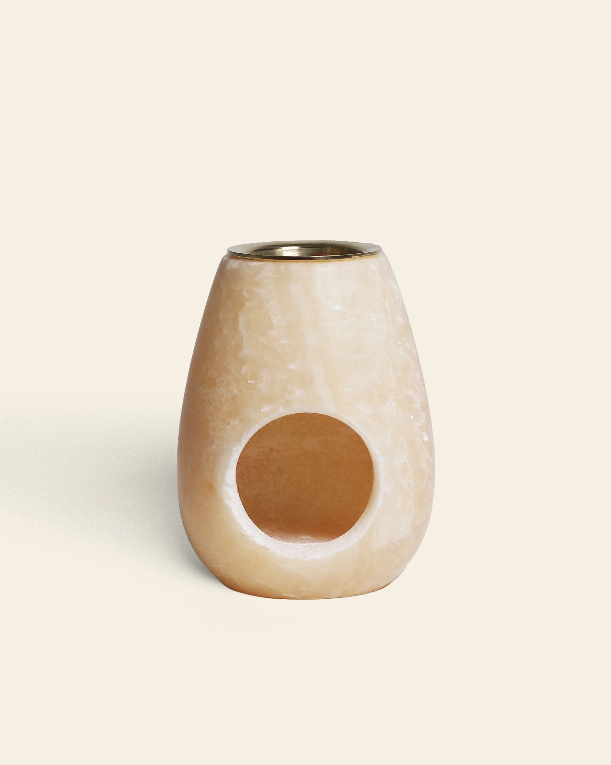 The stillgoods Eli Oil Burner, a beige oval candle holder with a circular front opening and metal-lined top, is ideal for diffusing your favorite scents. Shown against a plain light background.