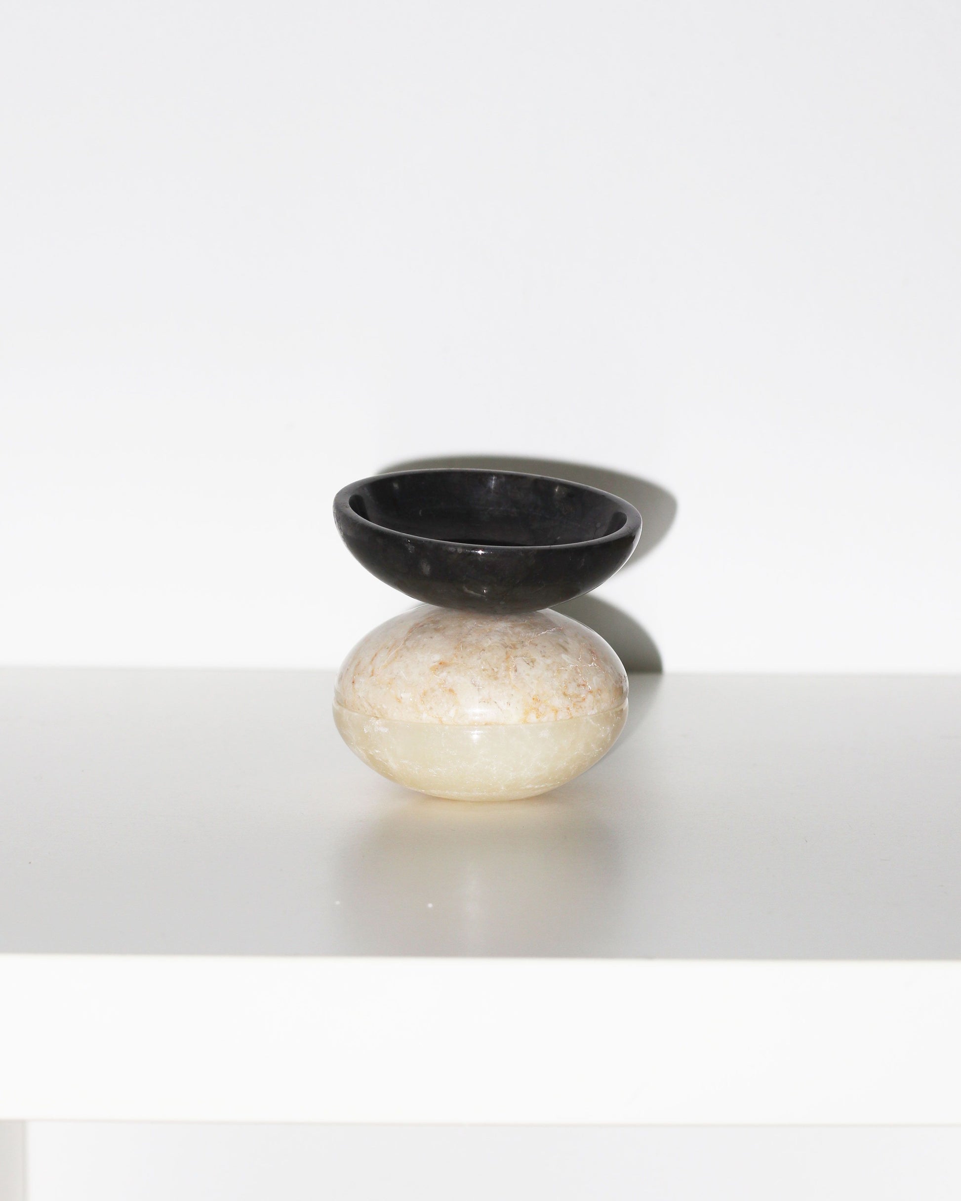The stillgoods Luna Dish is a small, round trinket dish with a beige base and black marble shallow bowl, displayed on a white surface against a plain white background.