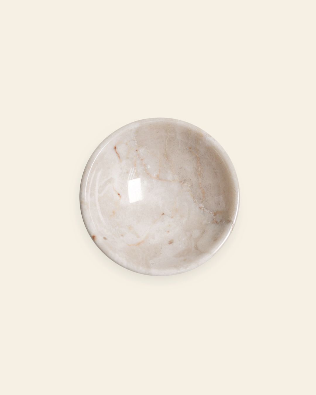 The stillgoods Luna Dish is a round, shallow marble catch-all featuring light beige and subtle brown veining, displayed against a plain off-white background.