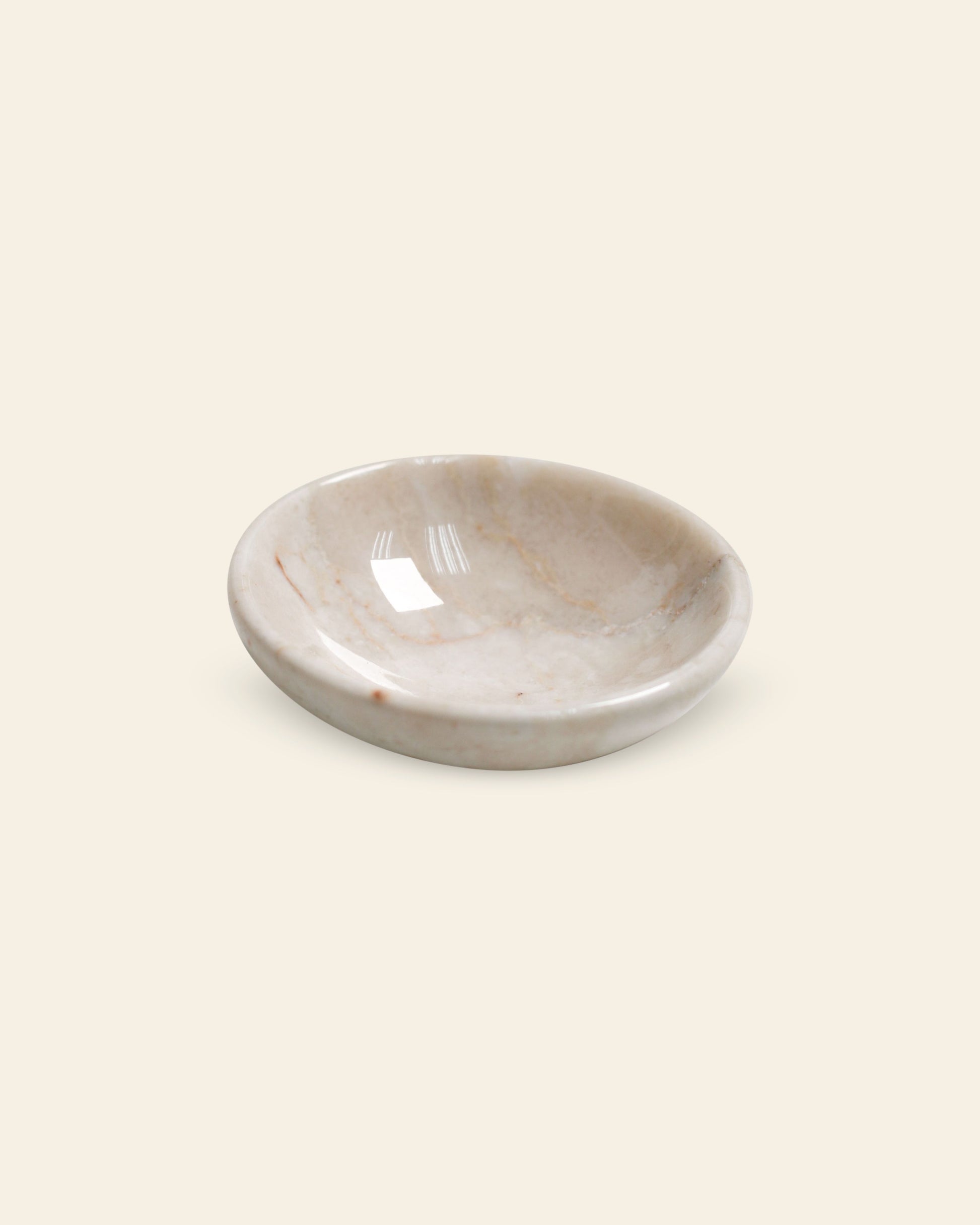 The stillgoods Luna Dish is a shallow, round marble trinket dish with a smooth, polished surface and subtle natural veining, shown against a plain light beige background.