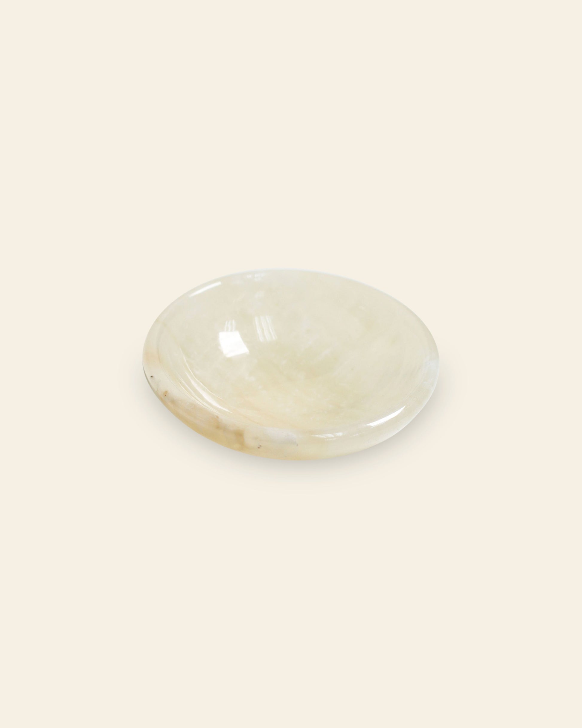 The stillgoods Luna Dish is a small, round trinket dish crafted from smooth, polished cream-colored stone by stillgoods, shown on an off-white background.