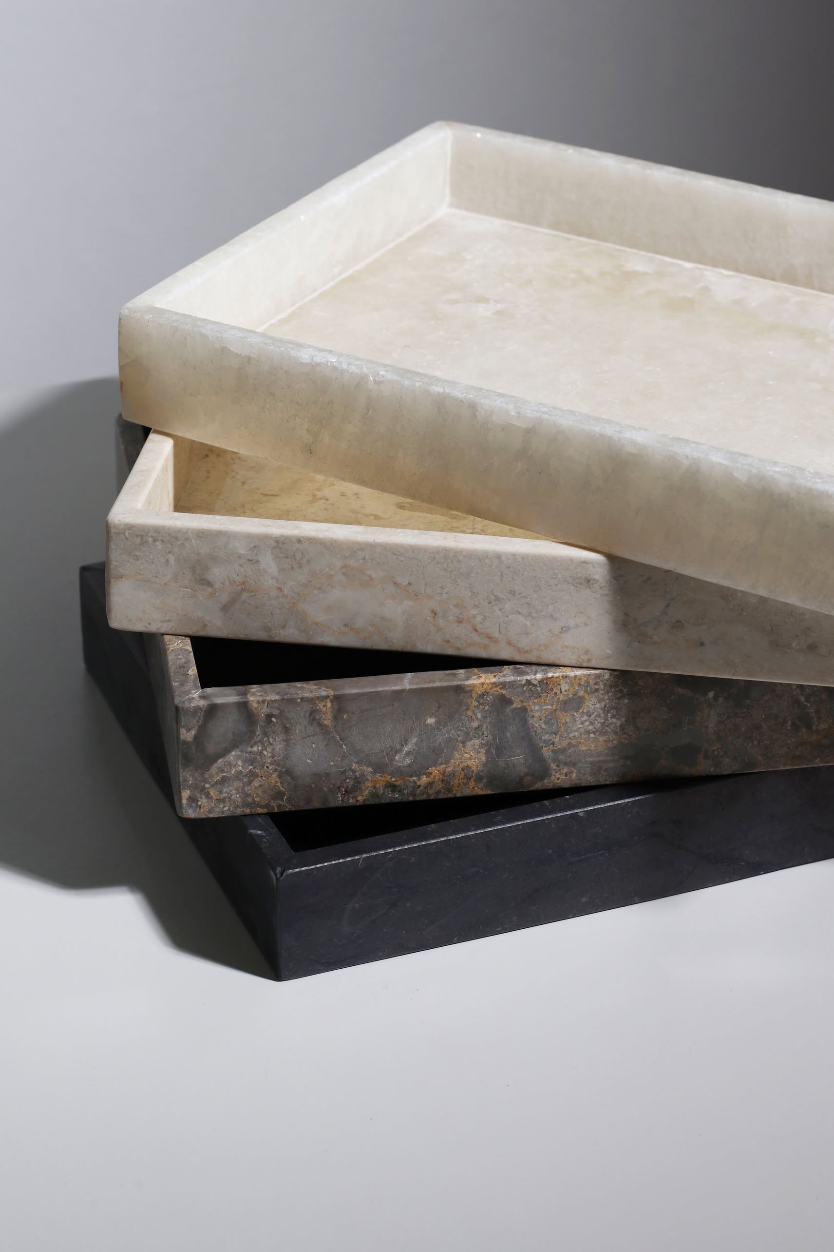 Four stillgoods Mini Valor Trays are stacked unevenly, highlighting their low-profile stone design. Ranging in color from cream to dark gray, theyre softly lit—perfect for neatly displaying your essentials.