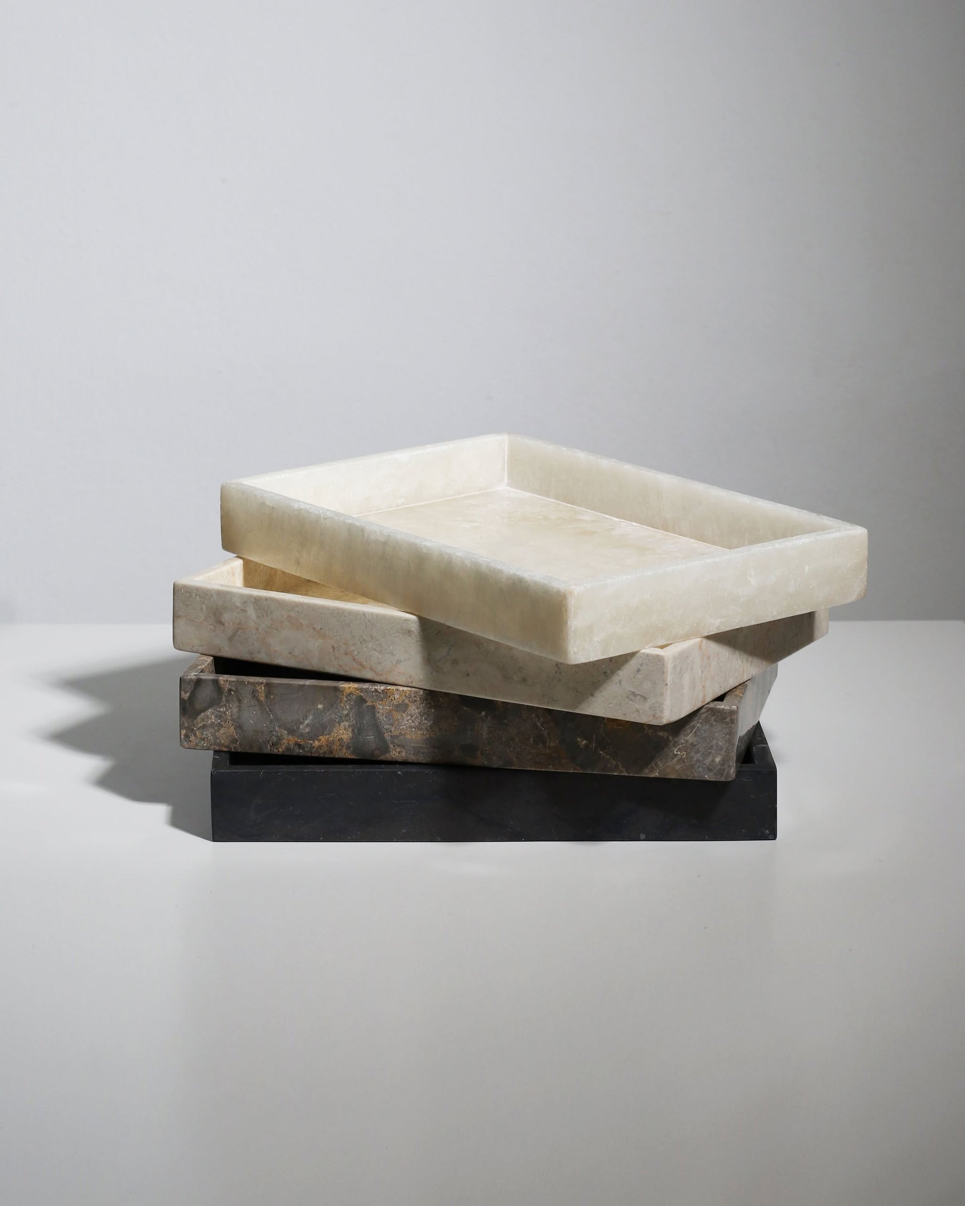 Three stillgoods Mini Valor Trays in white, beige, and dark gray are stacked on a white surface against a light gray background—their low profile keeps your essentials organized and within easy reach.