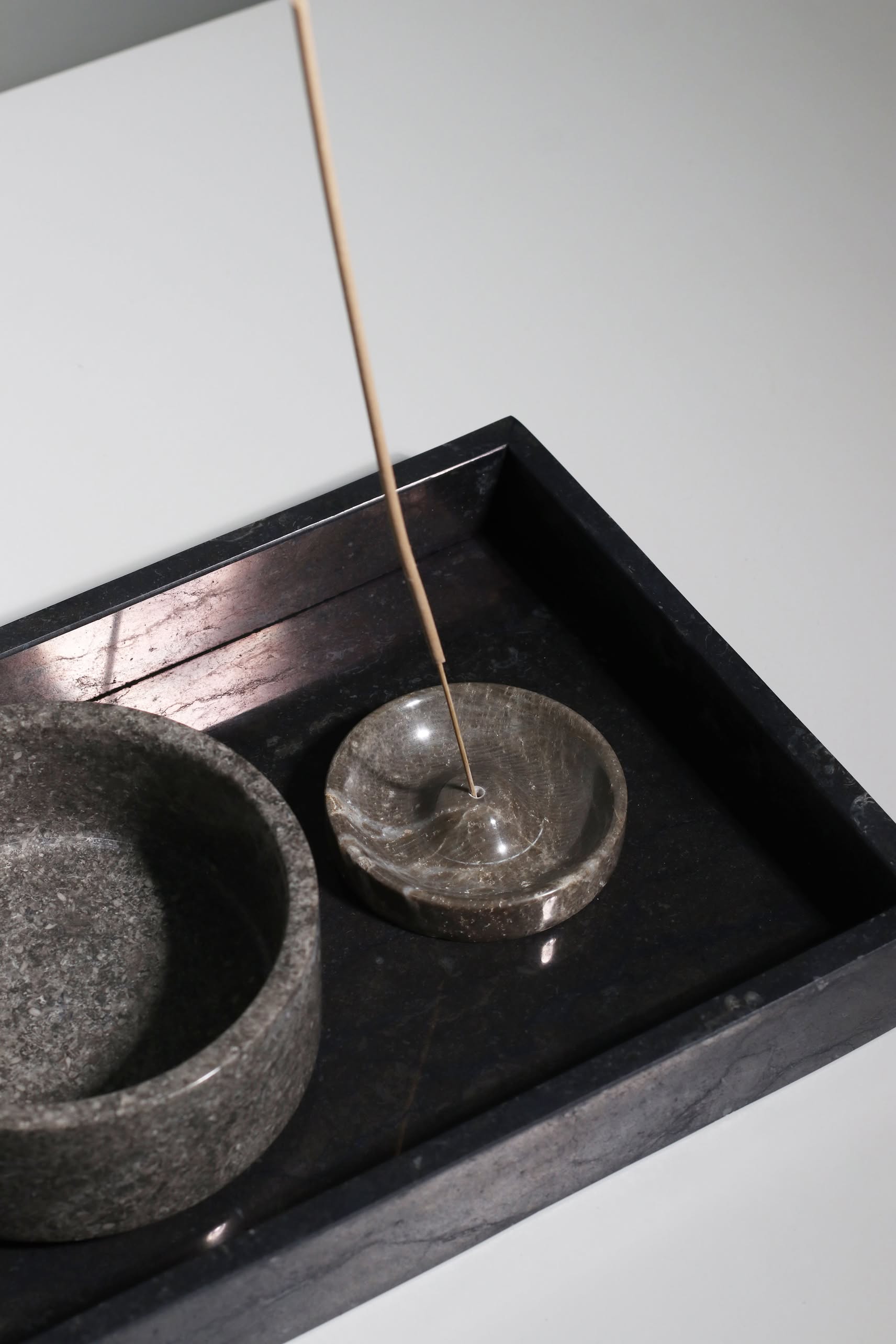A slender incense stick burns in a round stone holder on the stillgoods Mini Valor Tray, its low-profile design keeping essentials neat next to a larger empty stone bowl, all resting on a smooth, light surface.