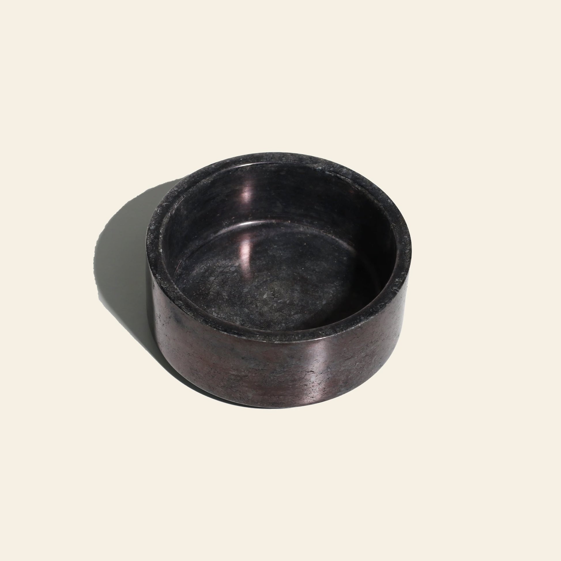 The stillgoods Tingkat Bowl, round and shallow with a dark marble-like finish, rests on a light beige surface and casts a soft left-side shadow. Its smooth texture and minimalist design reflect stillgoods’ signature style.