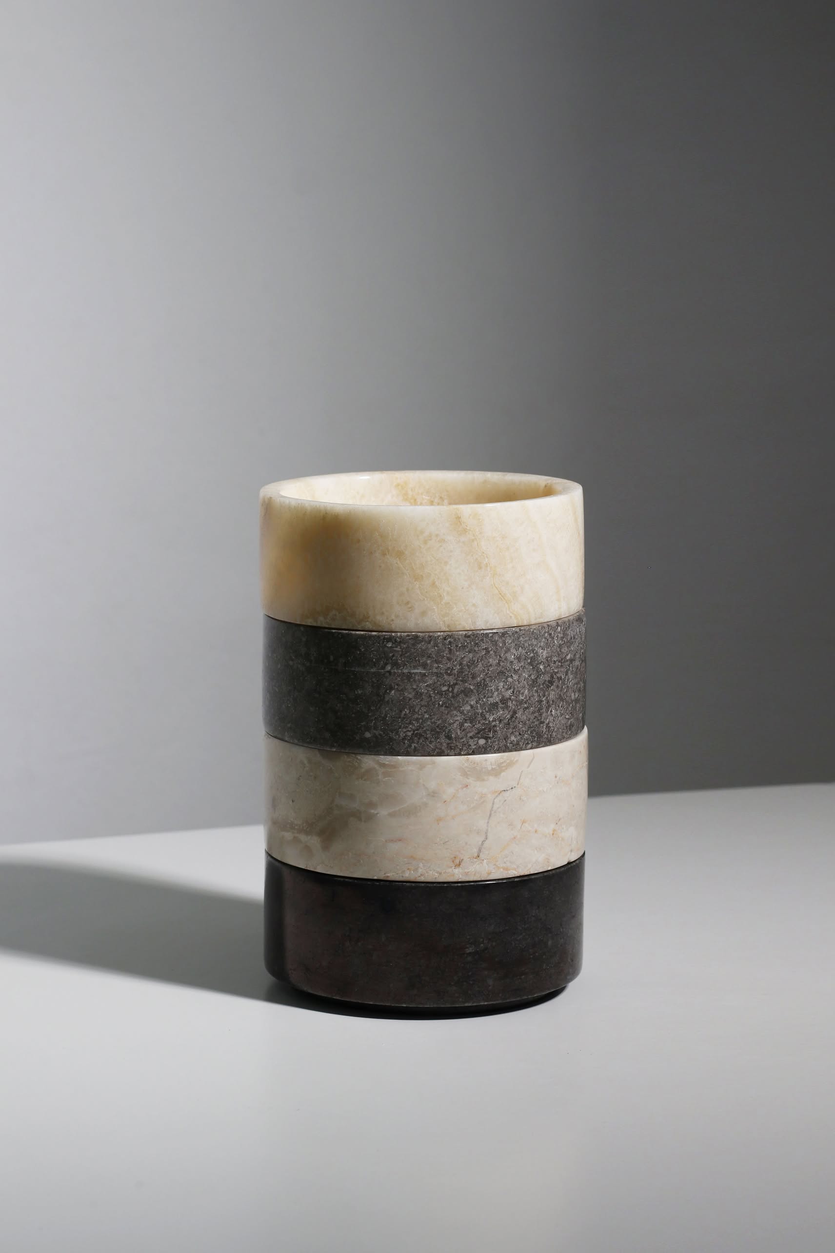 The stillgoods Tingkat Bowl by stillgoods features three horizontal bands in cream, gray, and black marble, displayed on a light gray surface with a plain gray background.