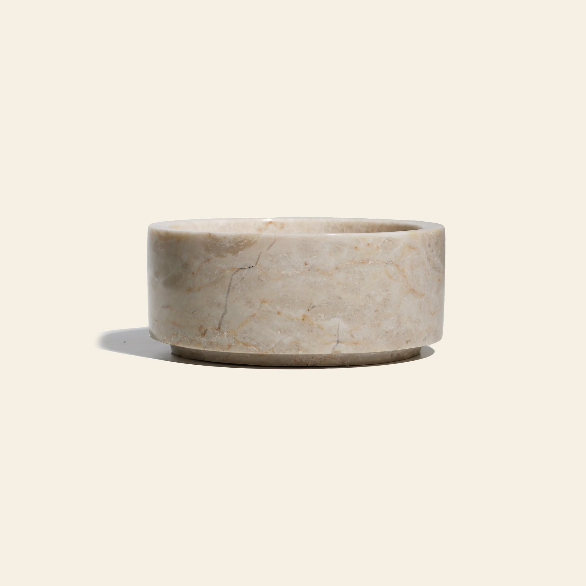 The stillgoods Tingkat Bowl, a round and shallow marble bowl with subtle veining, is shown against a plain light beige background, casting a soft shadow to the left.