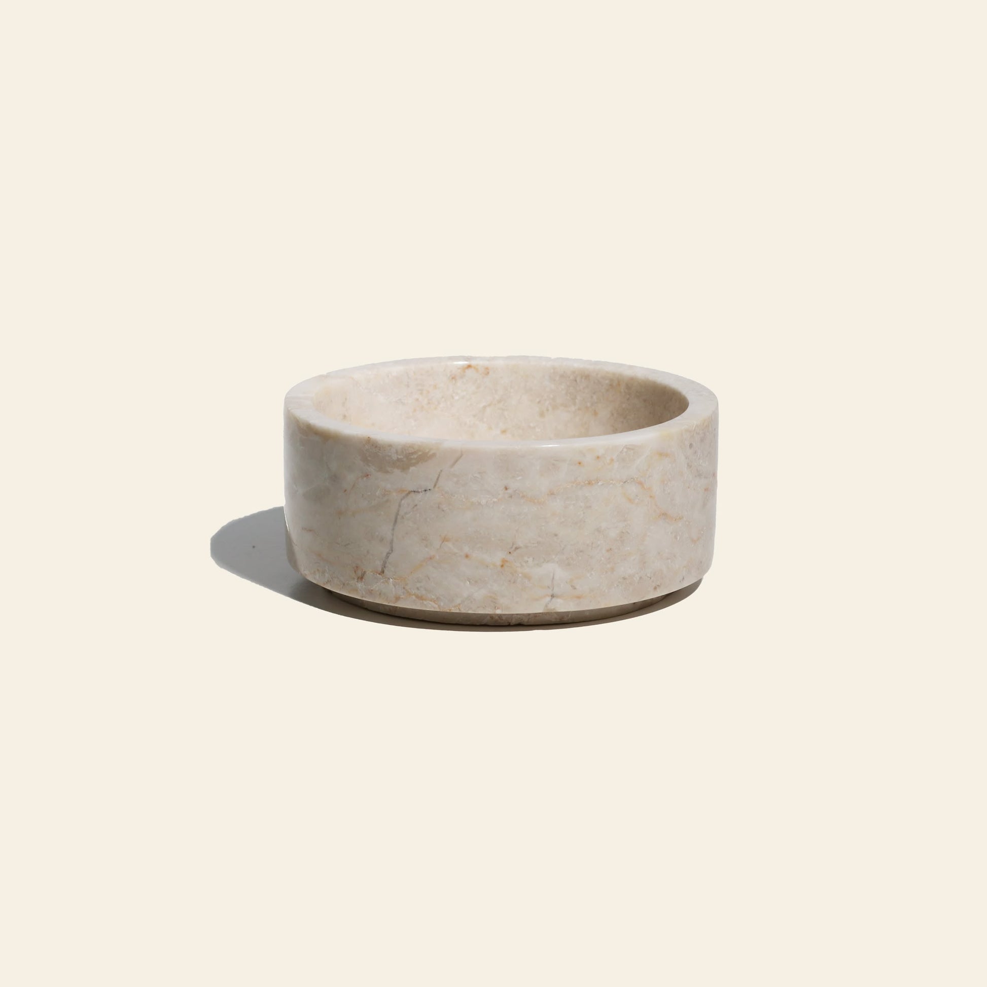 The stillgoods Tingkat Bowl is a round, light beige marble bowl with smooth sides and shallow depth, shown on a plain off-white background with a soft shadow.