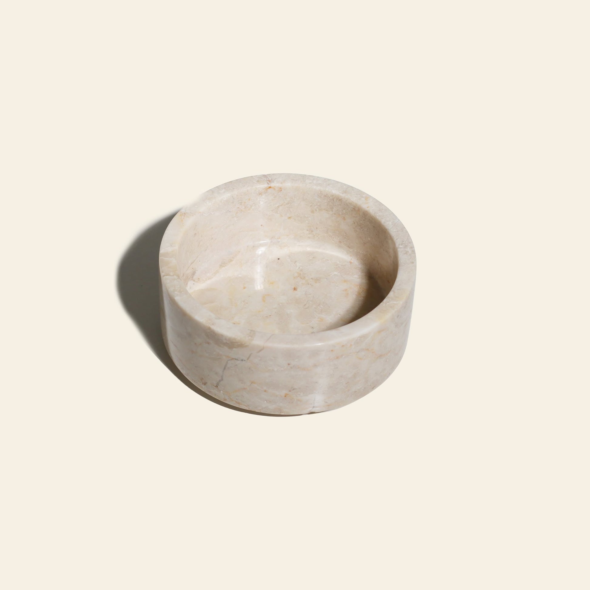 The stillgoods Tingkat Bowl is a round, shallow bowl crafted from light beige marble with subtle veining, shown on a plain light background with a soft shadow to the left.
