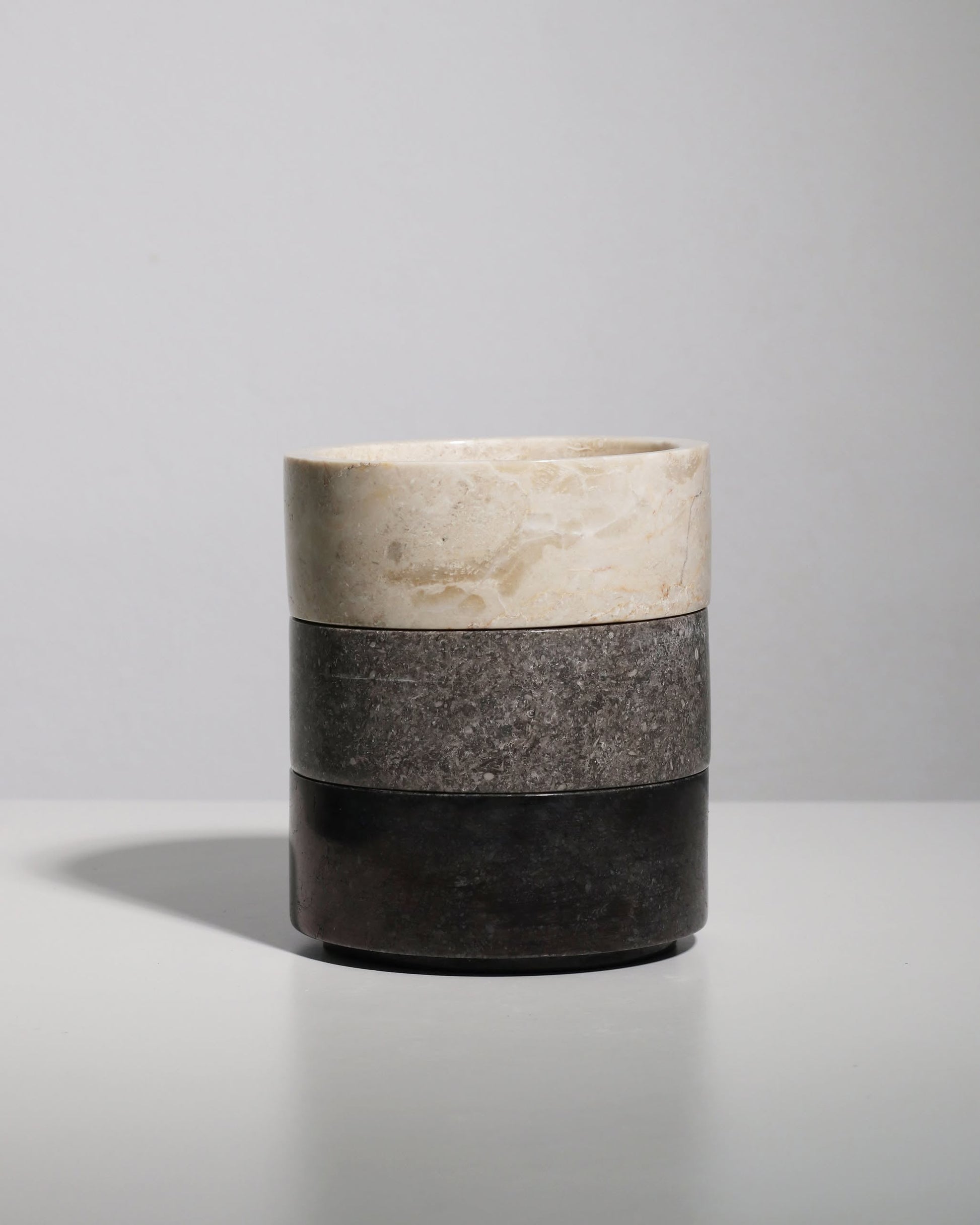 The stillgoods Tingkat Bowl features three stacked cylindrical sections in light beige, gray, and dark brown with a marble-like finish, displayed on a white surface against a plain light background.