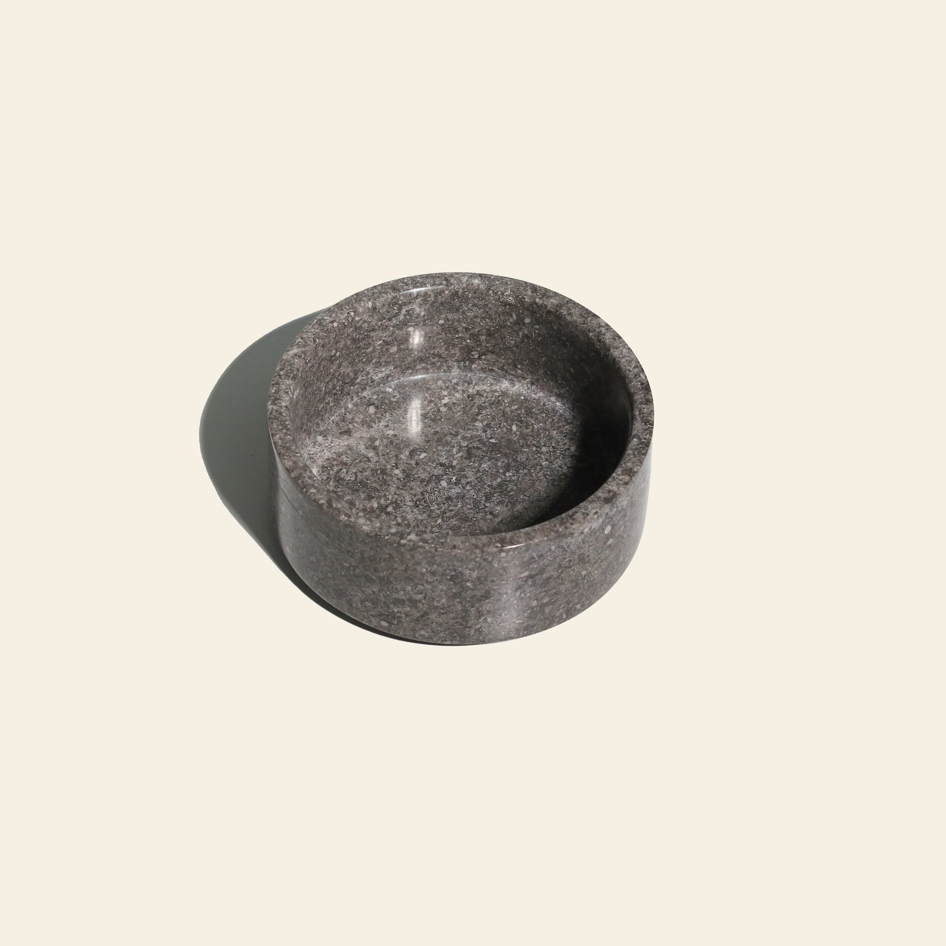 The stillgoods Tingkat Bowl, a round, shallow gray marble dish with a smooth texture, rests on a light beige surface and casts a soft shadow to the left.