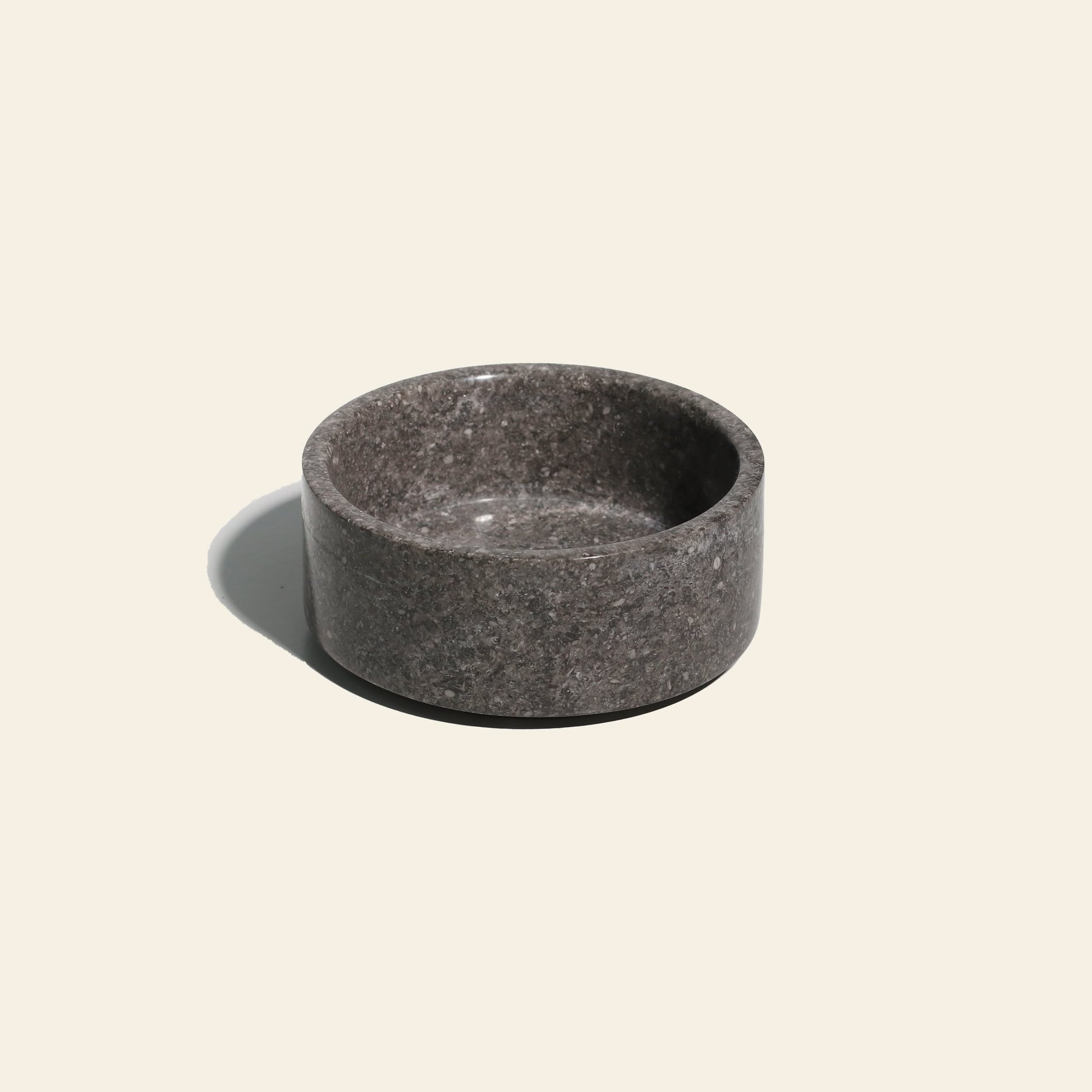 The stillgoods Tingkat Bowl, a round marble piece in dark gray with thick sides, rests on a light beige background and casts a soft shadow to the left.