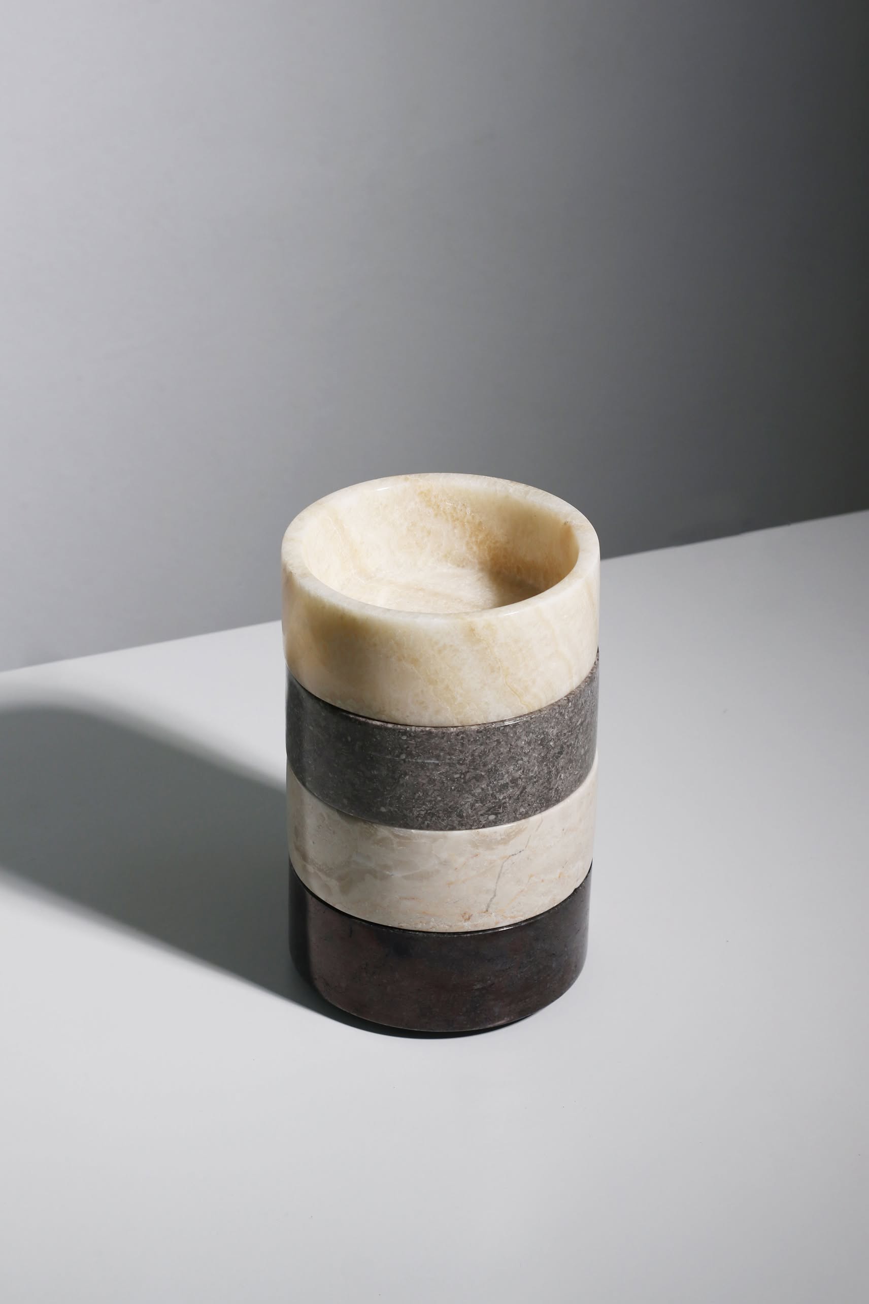 The stillgoods Tingkat Bowl is a cylindrical marble cup with four horizontal layers in beige, gray, and brown tones, featured on a white surface against a light gray background.