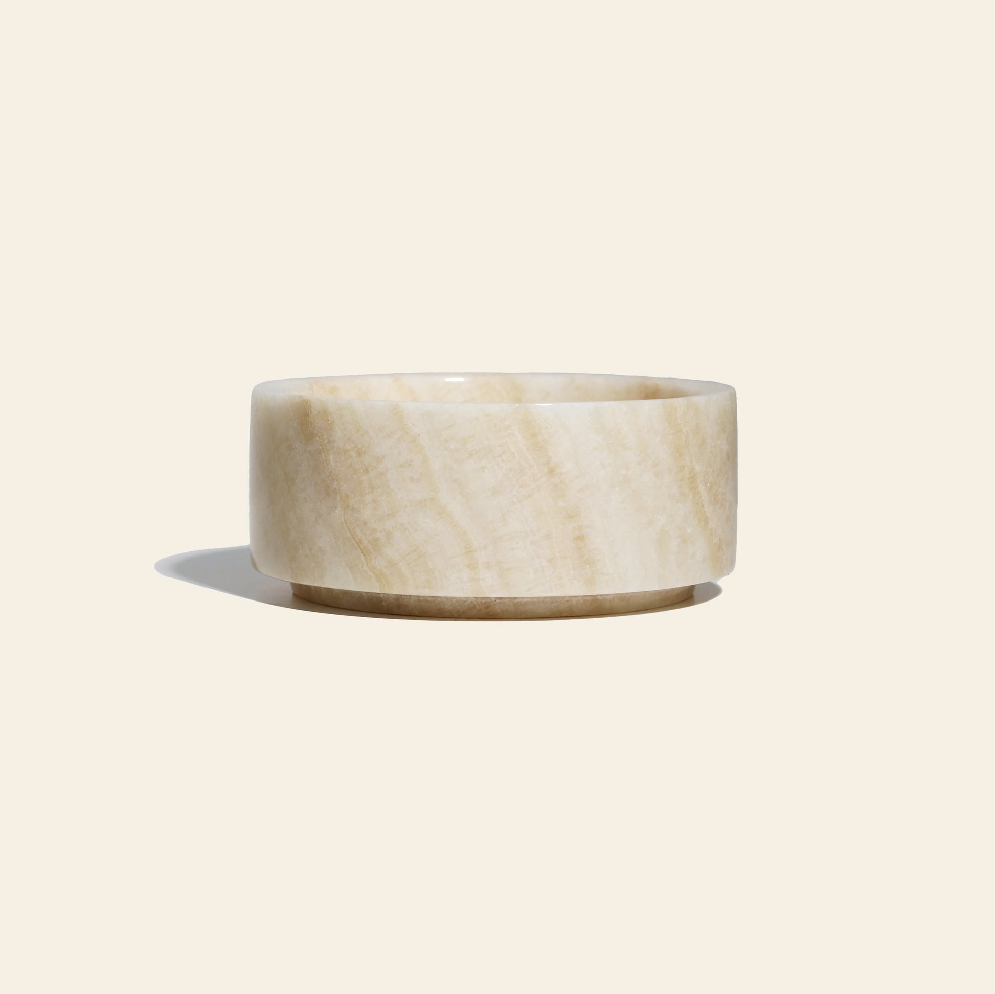 The stillgoods Tingkat Bowl, a round onyx marble bowl in light beige with a smooth, polished finish, is displayed on an off-white background with a soft shadow to the left.