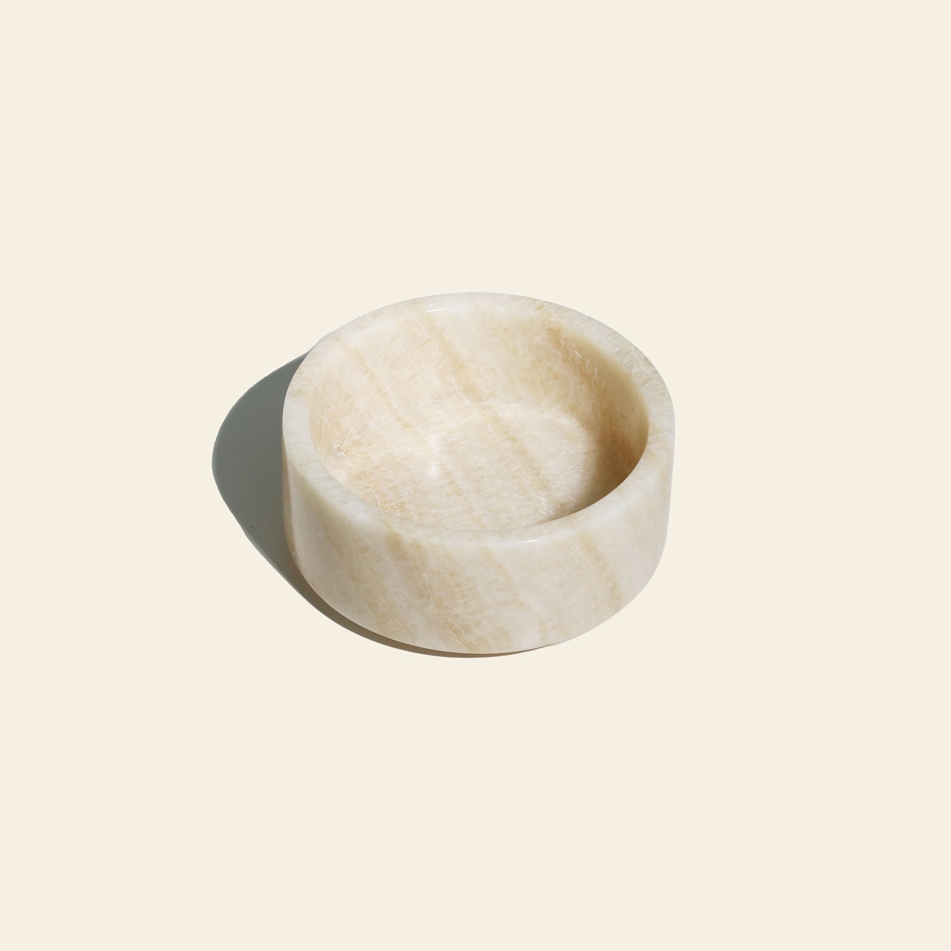 The stillgoods Tingkat Bowl, a small, round bowl crafted from polished light marble, is displayed on an off-white background with a shadow to the left.