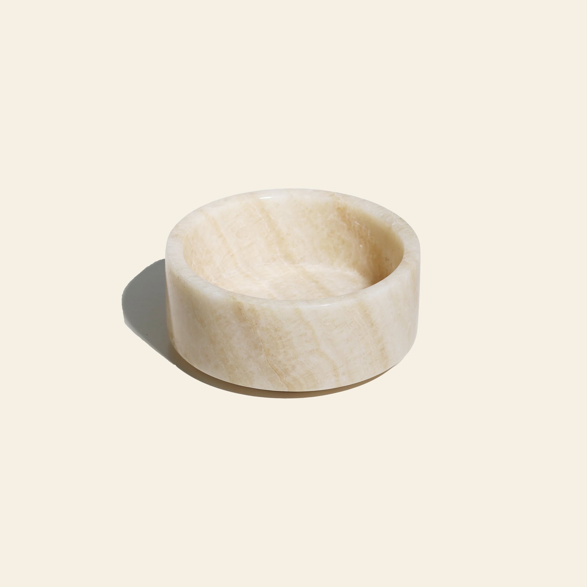 The stillgoods Tingkat Bowl is a round, shallow bowl crafted from polished light beige marble with subtle natural veining, shown on a pale background with a soft shadow to the left.